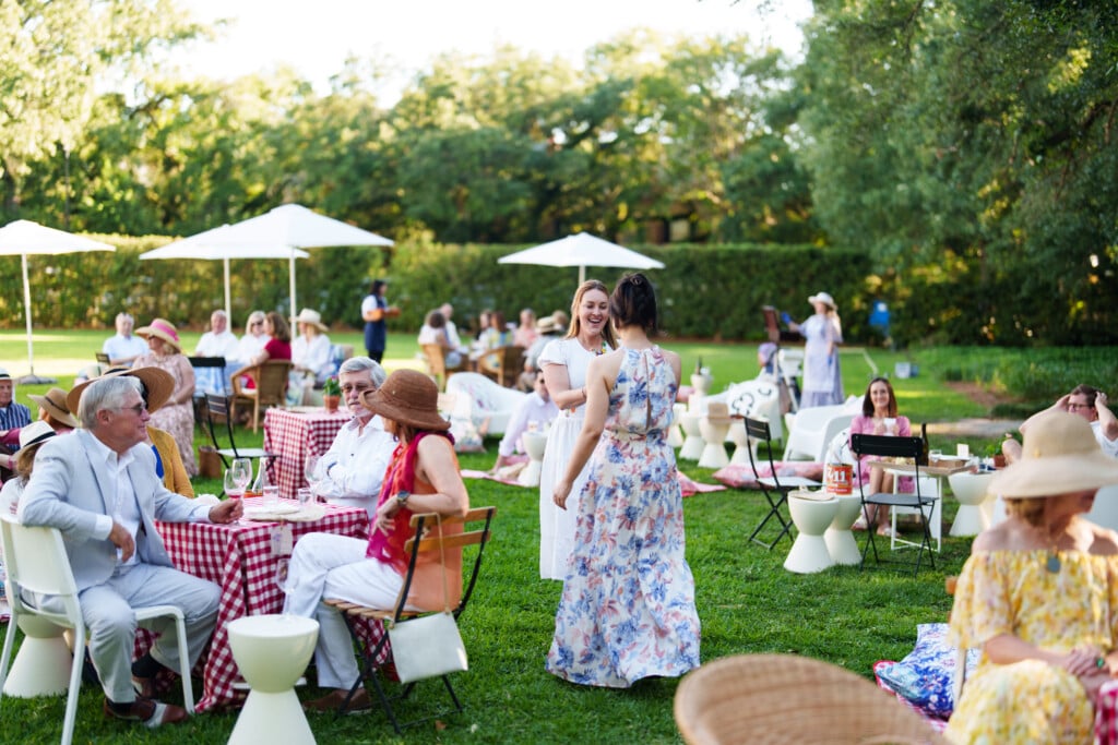 People outside in an open field with greenery and tables and chairs enjoying the Hilliard Art Museum Picnic in May