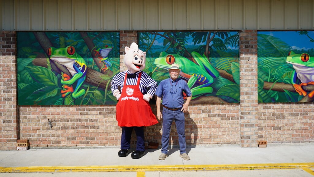 Robert Dafford and Piggly Wiggly mascot stand in front of Dafford's new frog mural painted at Piggly Wiggly in Rayne