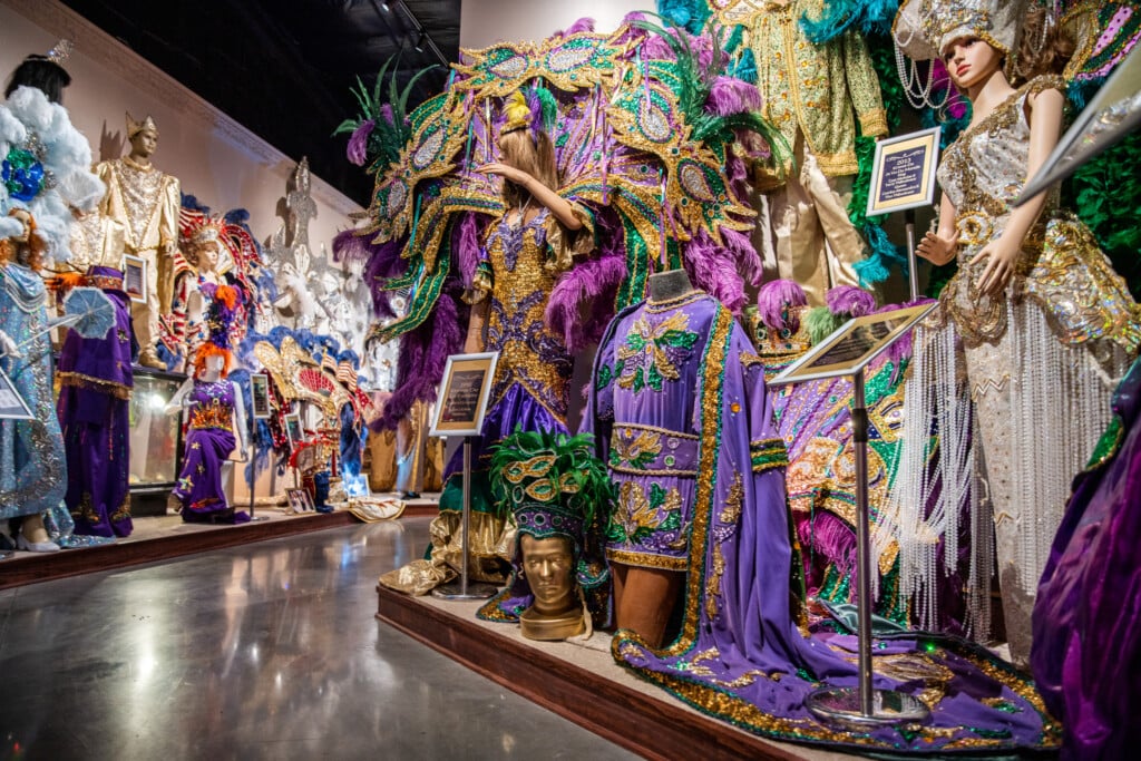Inside of Mardi Gras Museum of Imperial Calcasieu in Lake Charles, showing winding walkway surrounded by walls covered in costumes with display signs