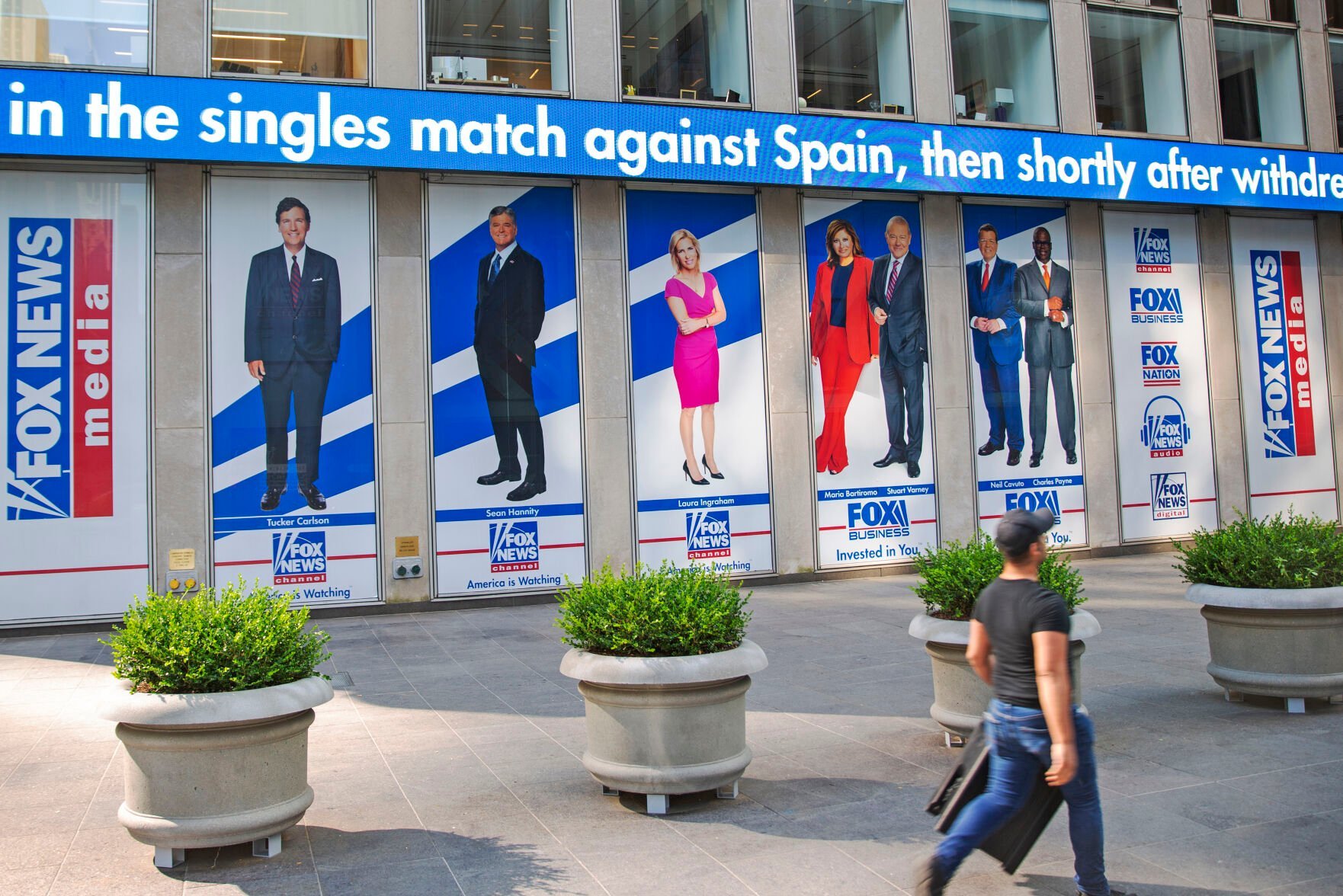 <p>FILE - A man walks past promotional posters outside Fox News studios at News Corporation headquarters in New York on Saturday, July 31, 2021. From left to right are hosts Tucker Carlson, Sean Hannity, Laura Ingraham, Maria Bartiromo, Stuart Varney, Neil Cavuto and Charles Payne. </p>