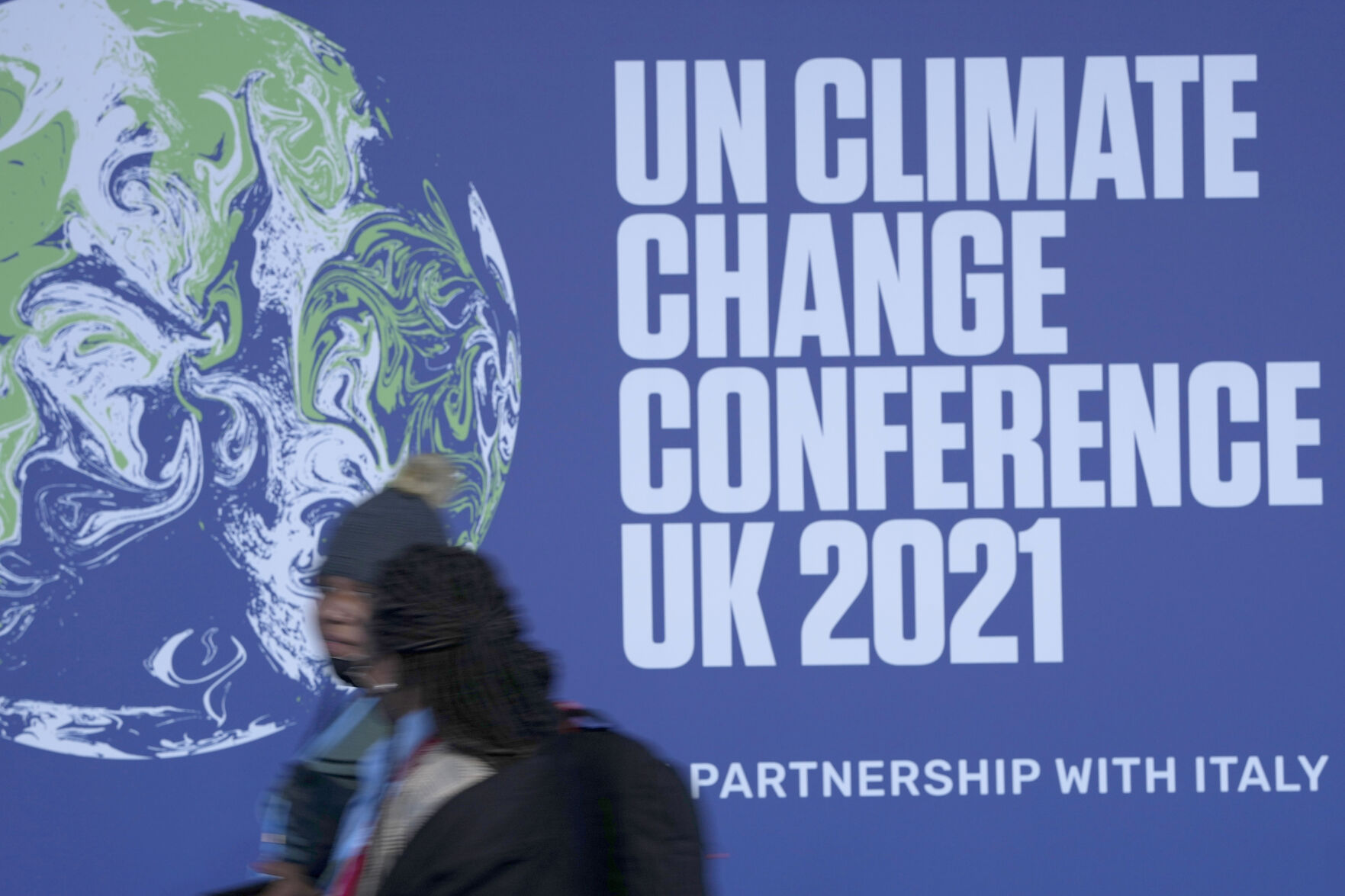 <p>FILE - Attendees walk past a banner at the venue of the COP climate conference in Glasgow, Scotland, on Oct. 29, 2021. On Friday, Nov. 5, The Associated Press reported on stories circulating online incorrectly claiming a photo showed jets used by attendees to get to the conference. In fact, the photo was taken during the 2013 Super Bowl in New Orleans. (AP Photo/Alastair Grant, File)</p>