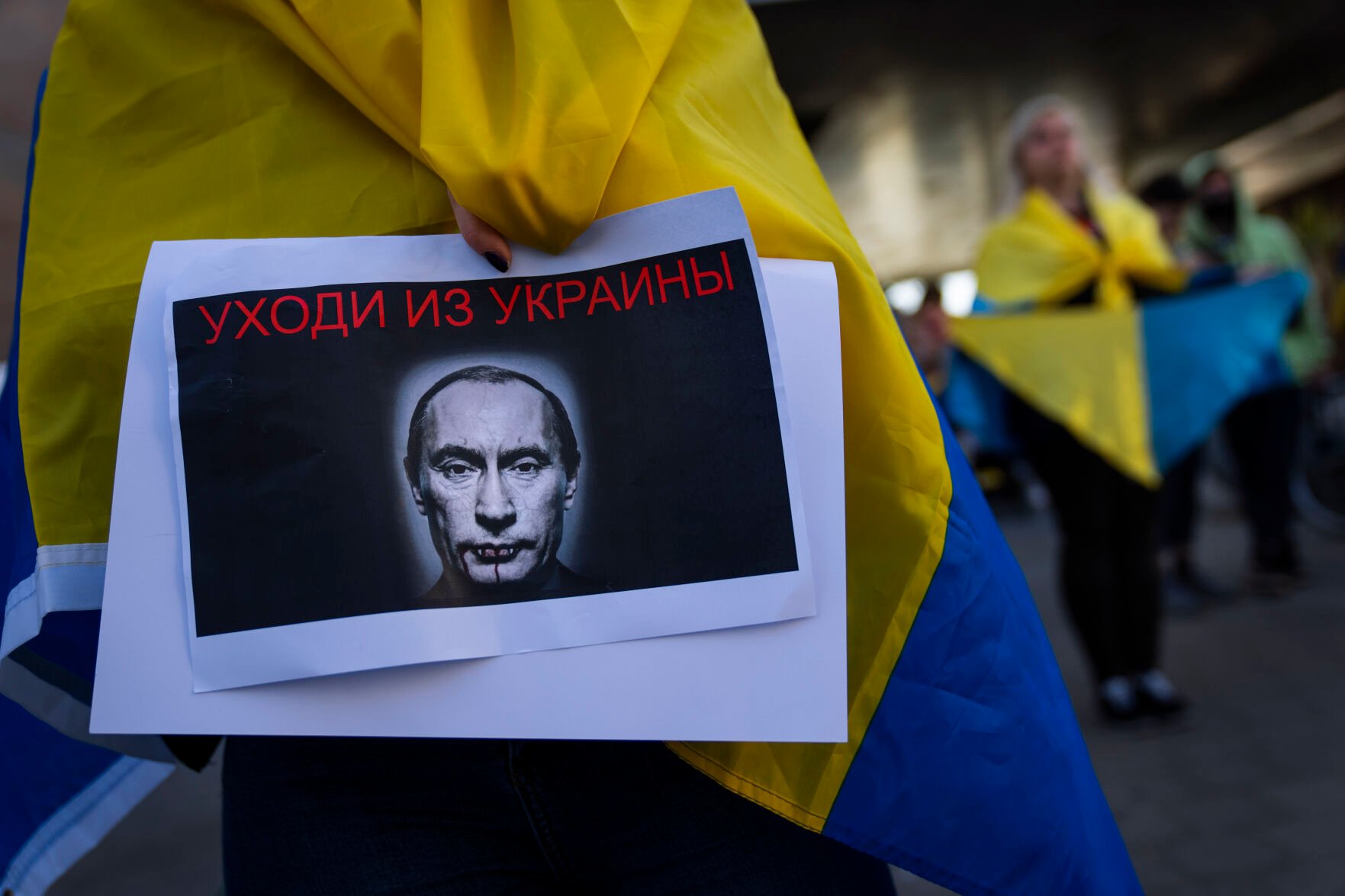 <p>A demonstrator holds a banner depicting Russian President Vladimir Putin during a pro-Ukraine protest outside the Russian Embassy, after Russian troops have launched their anticipated attack on Ukraine, in Tel Aviv, Israel, Thursday, Feb. 24, 2022. Sign in Russian reads "get out of Ukraine". (AP Photo/Oded Balilty)</p>