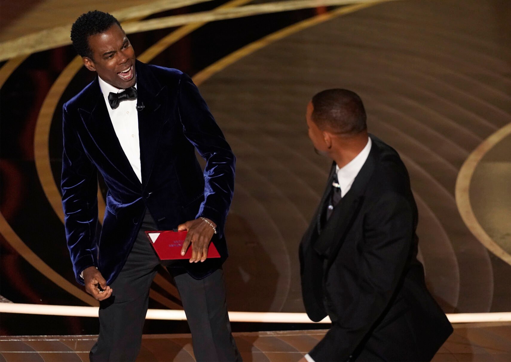 <p>presenter Chris Rock, left, reacts after being hit on stage by Will Smith while presenting the award for best documentary feature at the Oscars on Sunday, March 27, 2022, at the Dolby Theatre in Los Angeles. </p>