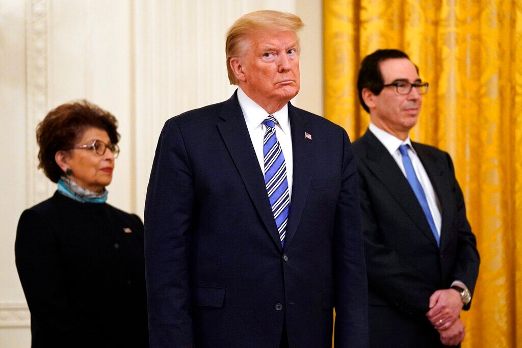 <p>In this April 28, 2020 file photo President Donald Trump, along with Jovita Carranza, administrator of the Small Business Administration, and Treasury Secretary Steven Mnuchin listen during an event about the Paycheck Protection Program used to support small businesses during the coronavirus outbreak, in the East Room of the White House in Washington. </p>