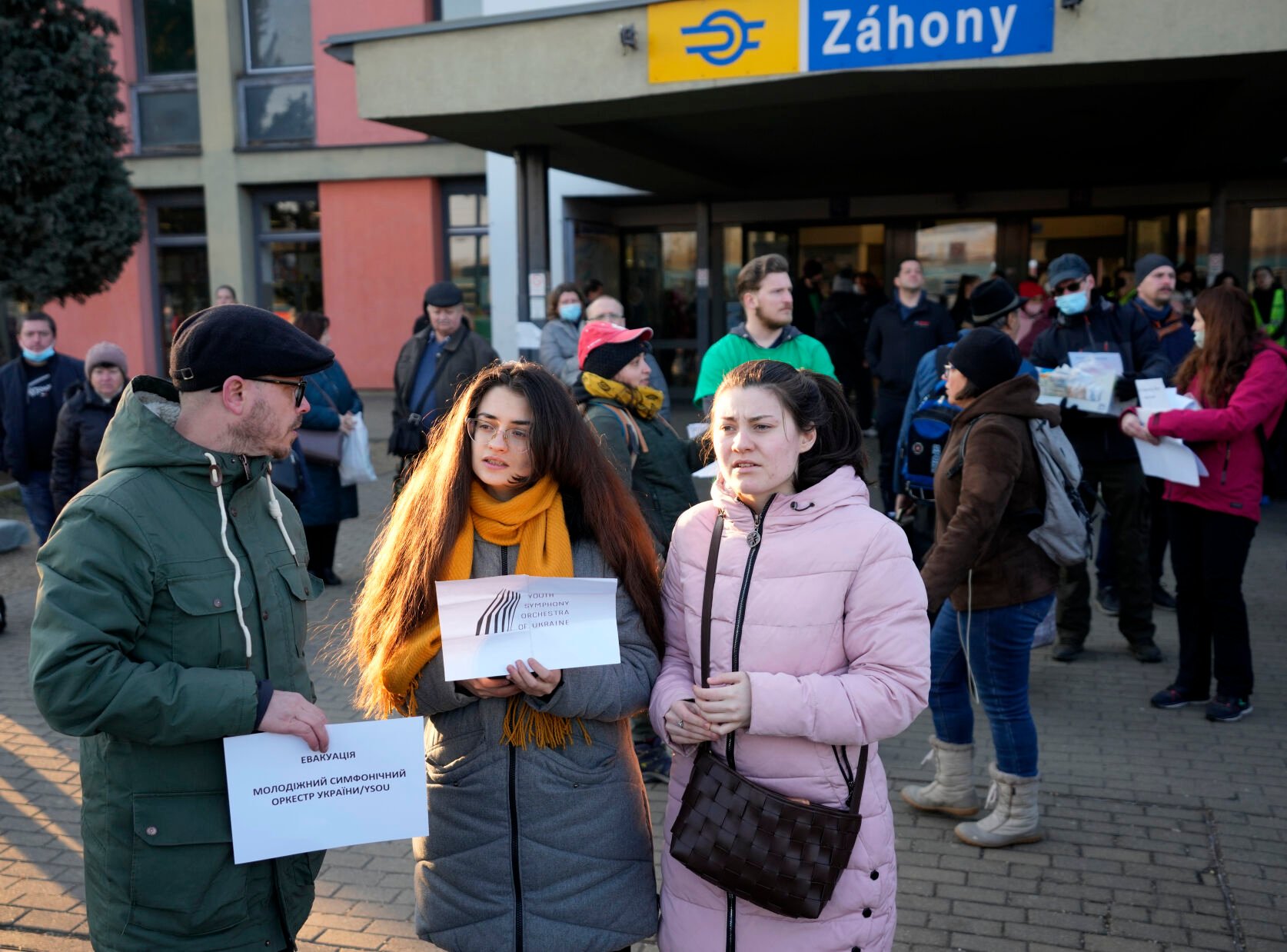 <p>Slovenian volunteer Uros Dokl, left, and violin player Myroslava Sherbina, center, wait for members of the Youth Symphonic Orchestra of Ukraine at the train station in Zahony, Hungary, Sunday, March 6, 2022. When Russia's invasion of Ukraine began and air raid sirens rang out in the embattled region of Donbas, Myroslava Sherbina rushed from her home and into a bomb shelter bringing only two of her possessions: the clothes on her back, and her violin. </p>