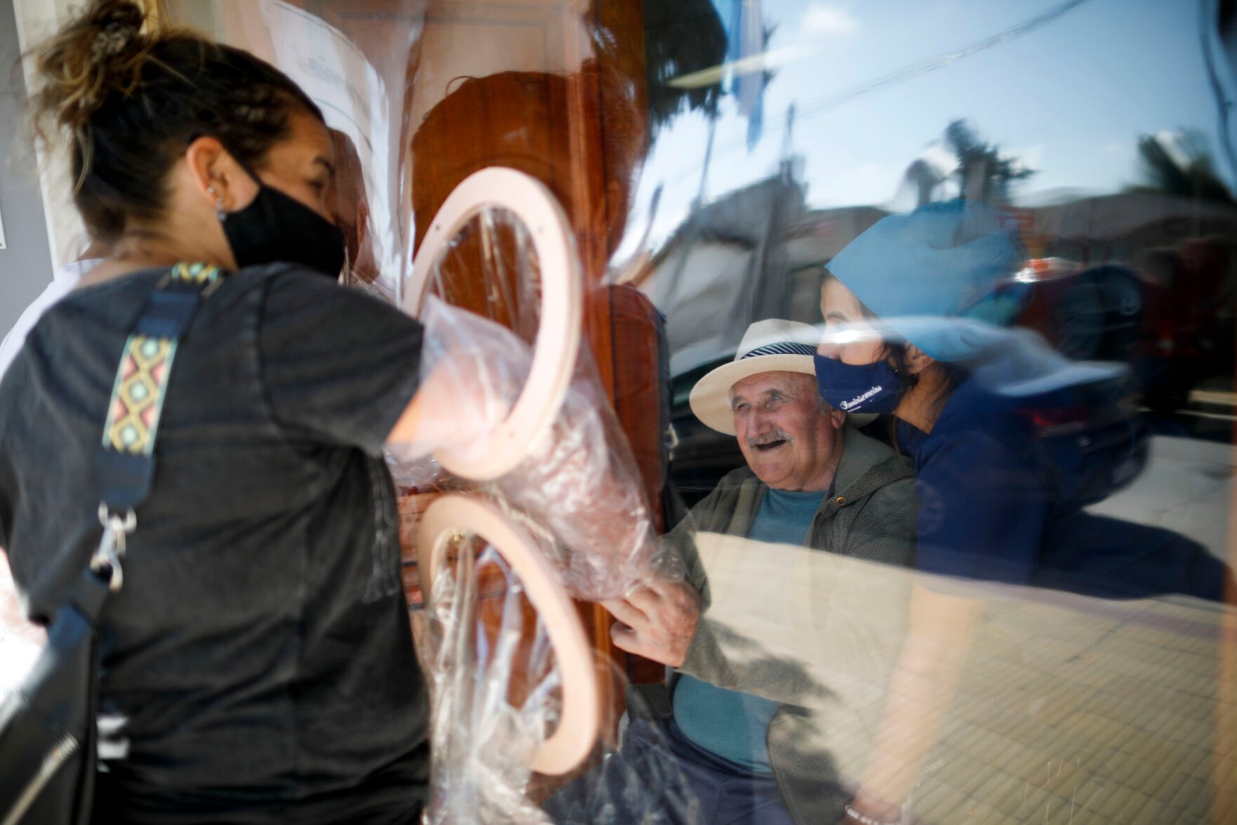 <p>Debora Aberastegui holds the hands of her father Pedro Aberastegui through a plastic sleeve at the Reminiscencias residence for the elderly in Tandil, Argentina, Monday, April 5, 2021. Residents here do not have physical contact with their families or leave the residence due to the COVID-19 pandemic, but stay active with group activities within the facility. </p>
