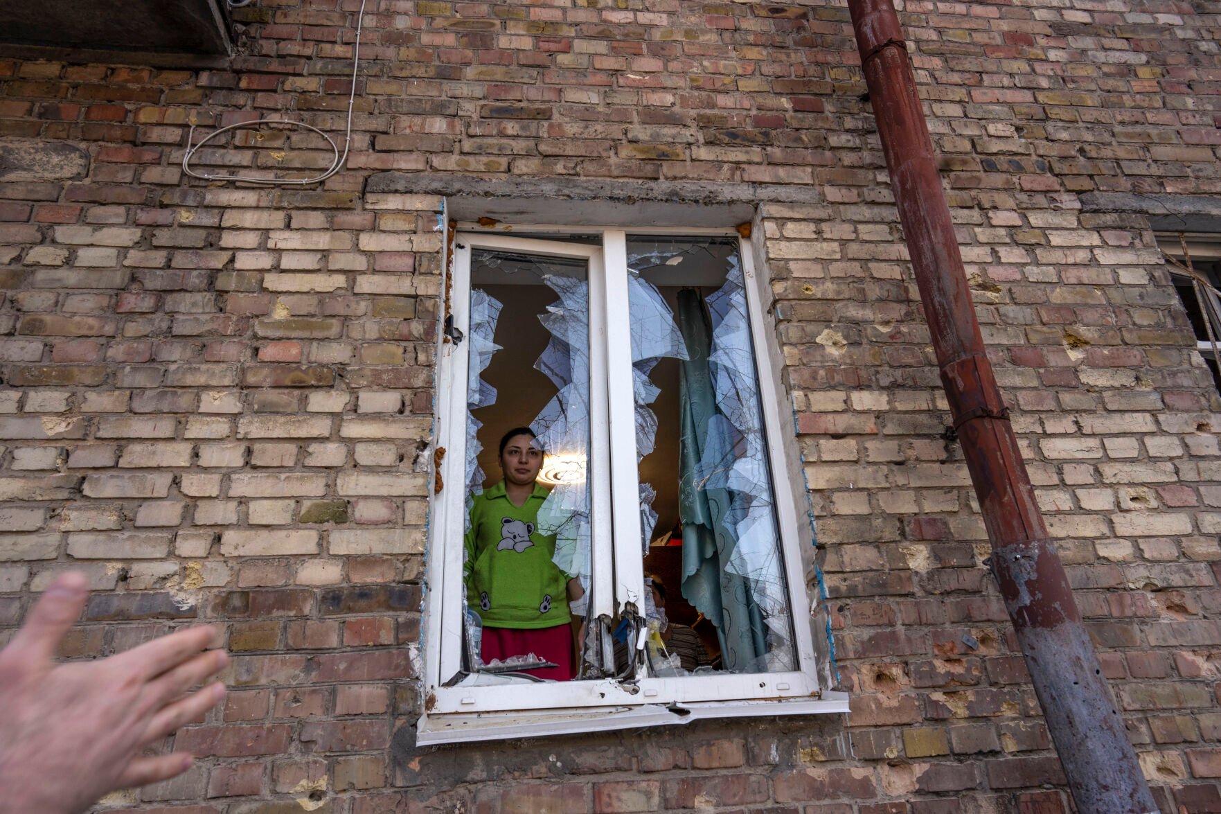 <p>Anna looks at the street thought a destroyed window inside her apartment, damaged by shelling, in Kyiv, Ukraine, Wednesday, March 23, 2022. </p>