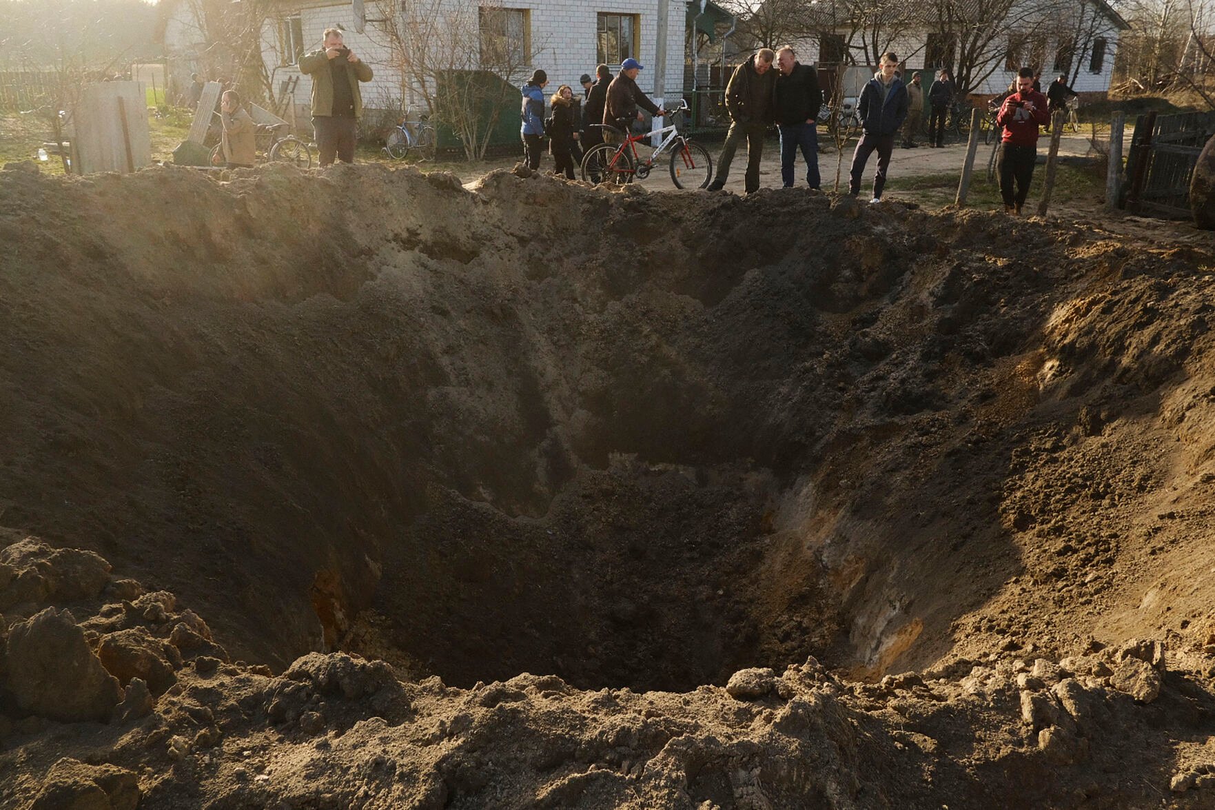 <p>People look at a crater of an explosion in a village of Horodnya, Chernihiv region, Ukraine, Thursday, April 14, 2022. The fluid nature of the conflict, which has seen fighting shift away from areas around the capital and heavily toward Ukraine's east, has made the task of reaching hungry Ukrainians especially difficult. (AP Photo/George Ivanchenko)</p>