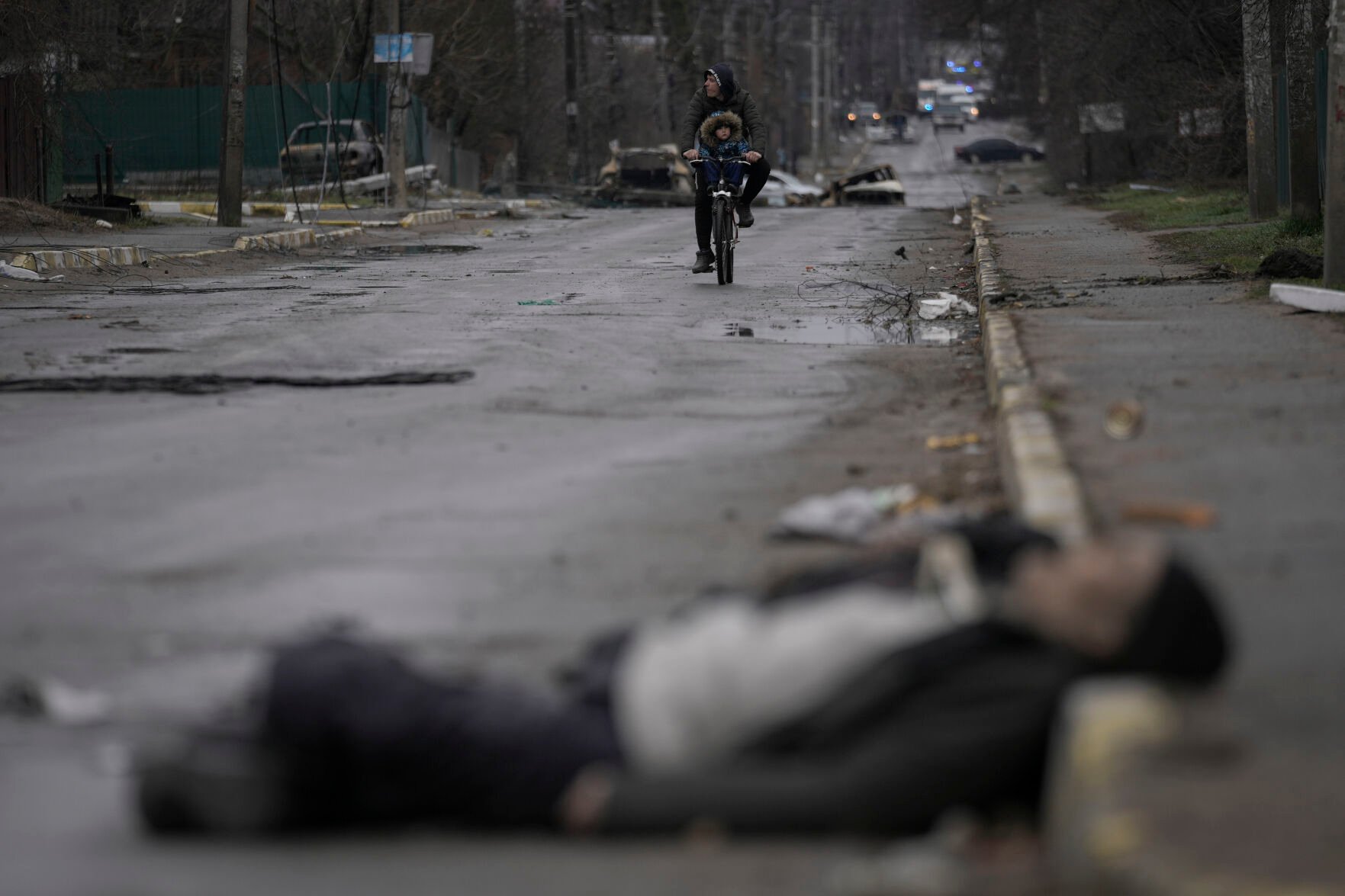 <p>FILE - A man and child ride on a bicycle as bodies of civilians lie in the street in the formerly Russian-occupied Kyiv suburb of Bucha, Ukraine, Saturday, April 2, 2022. (AP Photo/Vadim Ghirda, File)</p>