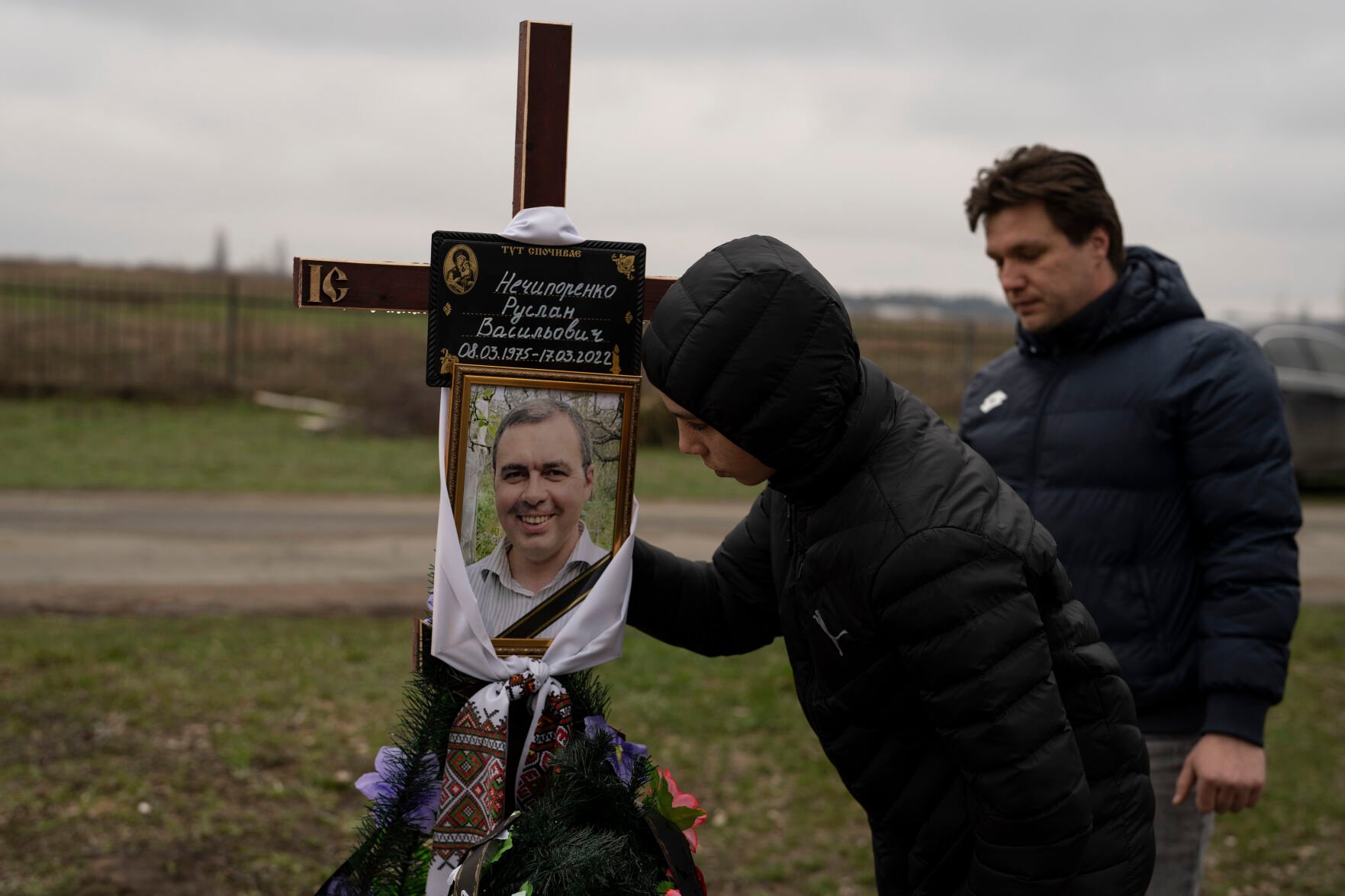 <p>Yura Nechyporenko, 15, kisses the pictures of his father Ruslan Nechyporenko in front of his uncle Andriy Nechyporenko, at the cemetery in Bucha, on the outskirts of Kyiv, Ukraine, on Thursday, April 21, 2022. </p>