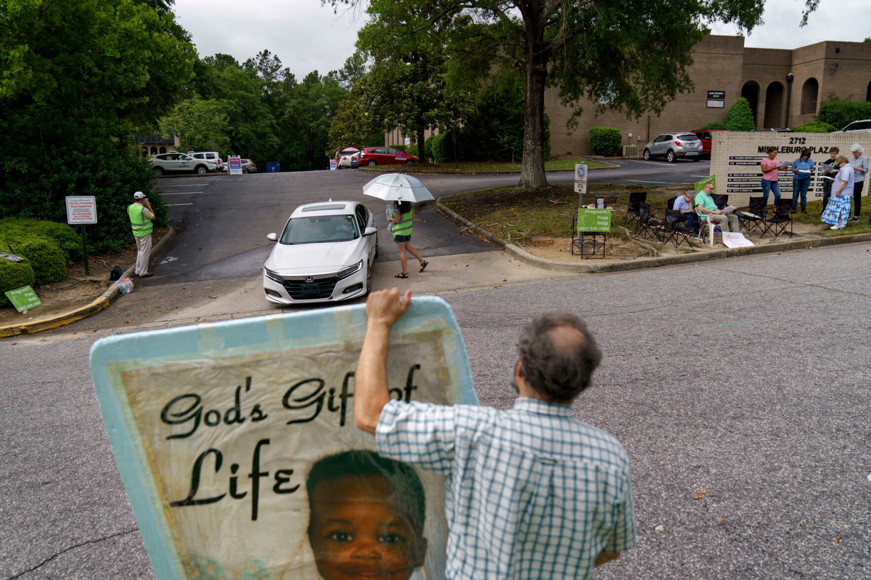 <p>Anti-abortion protester Steven Lefemine, holds a sign as the anti-abortion group, A Moment of Hope, wearing green vests, tries to talk with patients arriving for abortion appointments at Planned Parenthood next to a group of Catholics praying off to the side, Friday, May 27, 2022, in Columbia, S.C. </p>