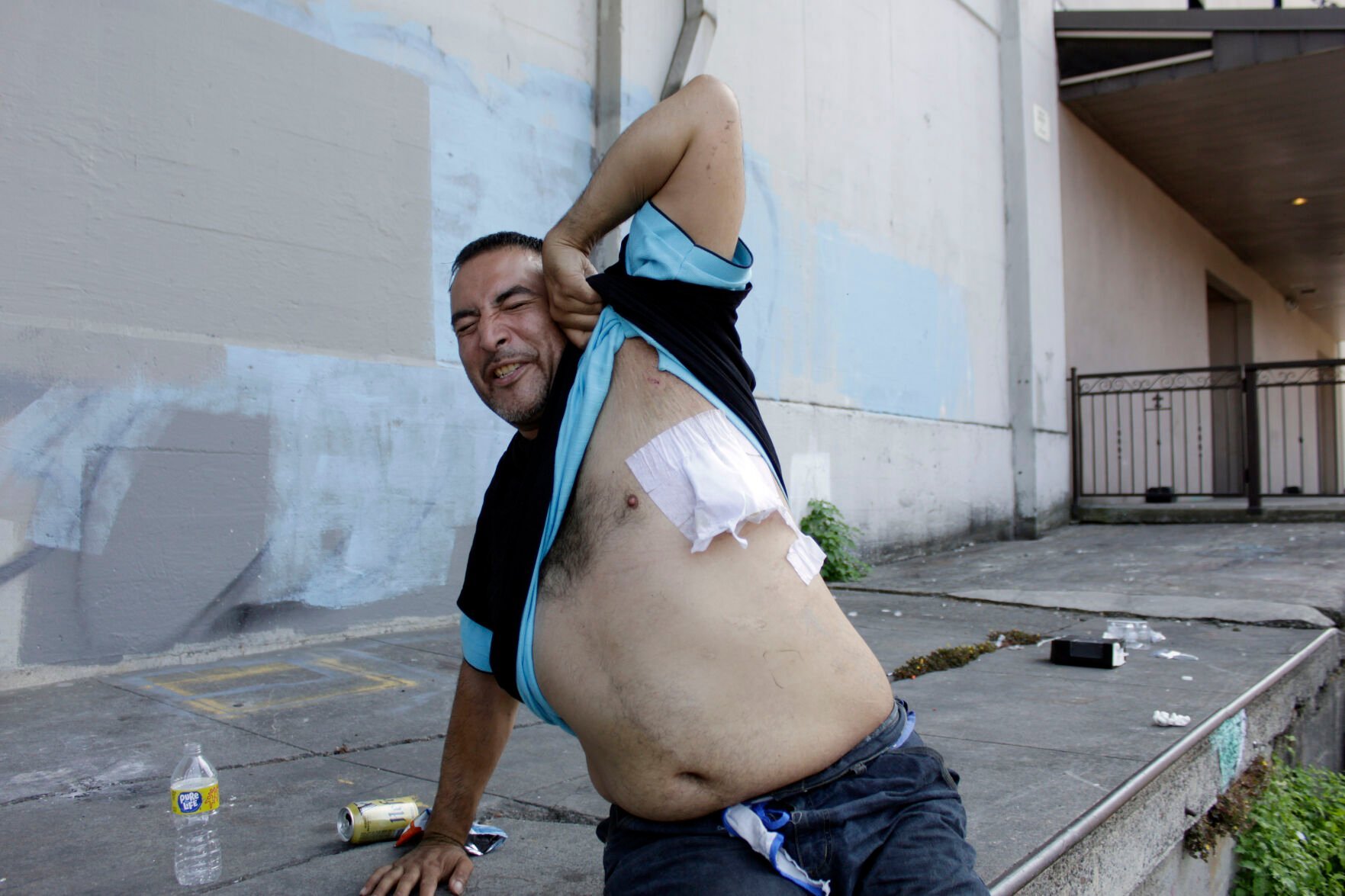 <p>Jeremiah King, who is transitioning out of homelessness, grimaces in pain as he shows the bandage on a gunshot wound as he sits on the street after his hospital release in Portland, Ore., on July 27, 2022. </p>