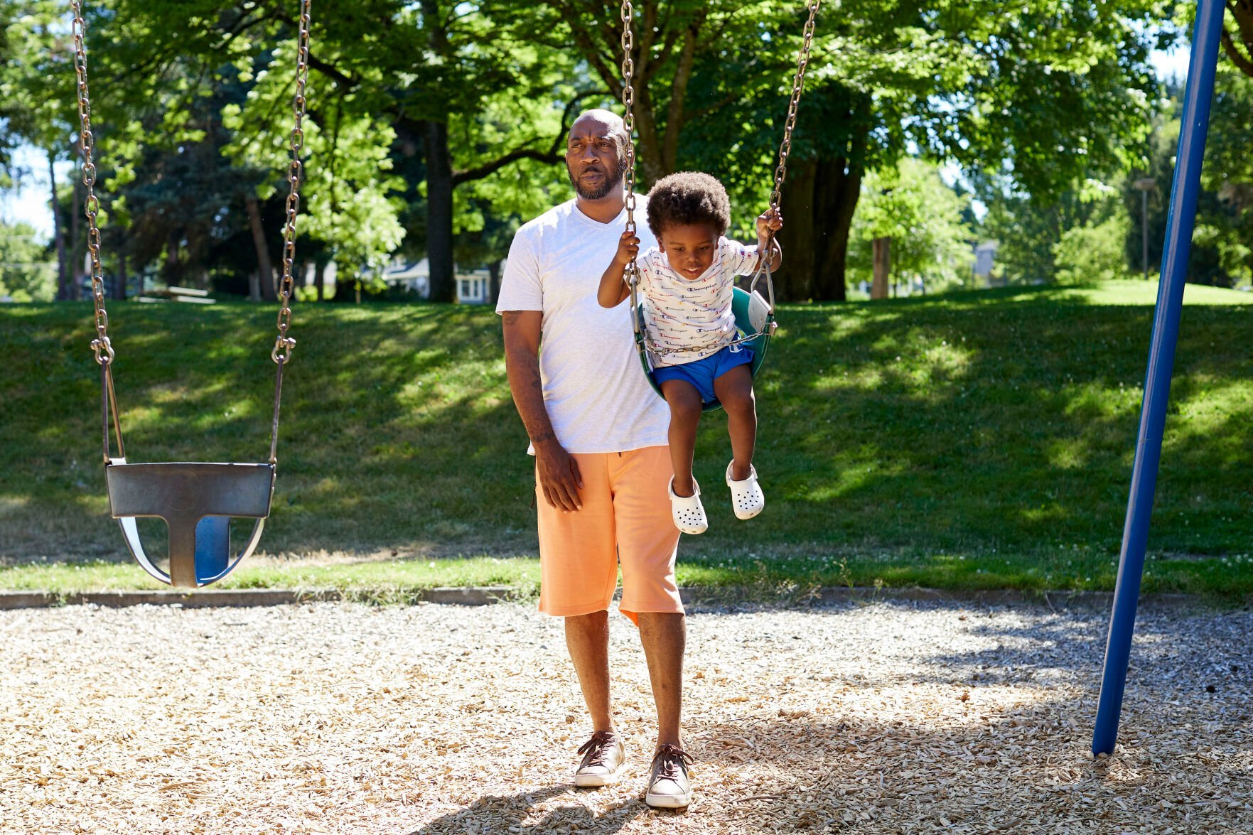 <p>Royal Harris, pushes his grandson, Carter, 2, on swings at Woodlawn Park in Portland, Ore., Wednesday, July 20, 2022. Harris, who has lost friends and family to Portland's gang violence, says he supports diverting resources from cold case units to address spiking gun violence in the city. </p>