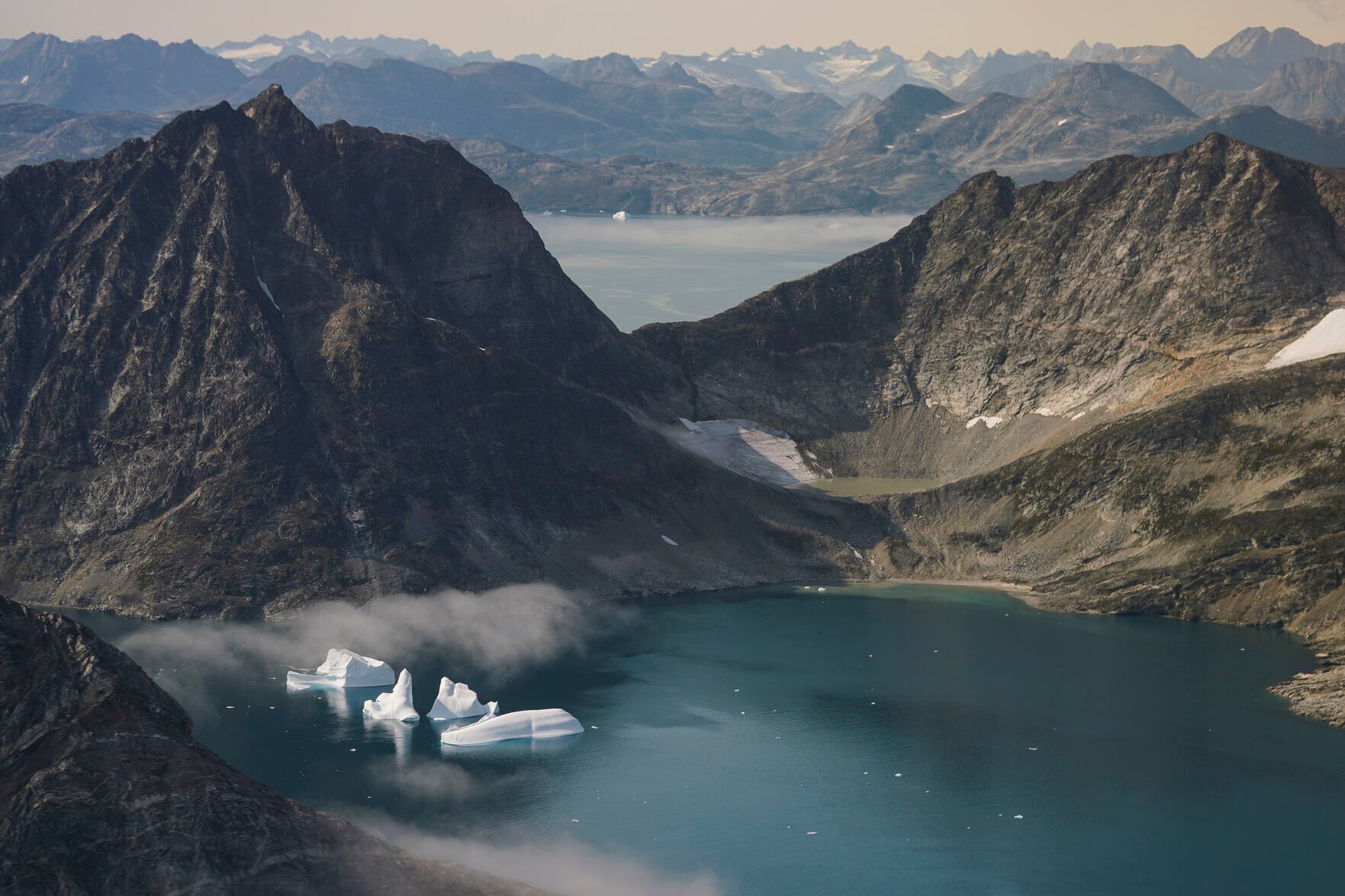 <p>FILE - Icebergs are seen through a window of an airplane carrying NASA scientists as they fly on a mission to track melting ice in eastern Greenland on Aug. 14, 2019. Zombie ice from the massive Greenland ice sheet will eventually raise global sea level by at least 10 inches (27 centimeters) on its own, according to a study released Monday, Aug. 29, 2022. Zombie or doomed ice is still attached to thicker areas of ice, but it’s no longer getting fed by those larger glaciers. (AP Photo/Mstyslav Chernov, File)</p>