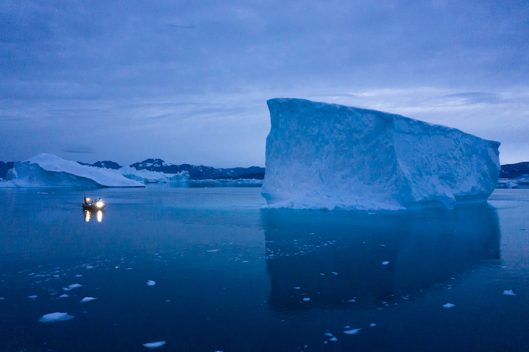 <p>FILE - A boat navigates at night next to large icebergs in eastern Greenland on Aug. 15, 2019. Zombie ice from the massive Greenland ice sheet will eventually raise global sea level by at least 10 inches (27 centimeters) on its own, according to a study released Monday, Aug. 29, 2022. Zombie or doomed ice is still attached to thicker areas of ice, but it’s no longer getting fed by those larger glaciers. (AP Photo/Felipe Dana, File)</p>