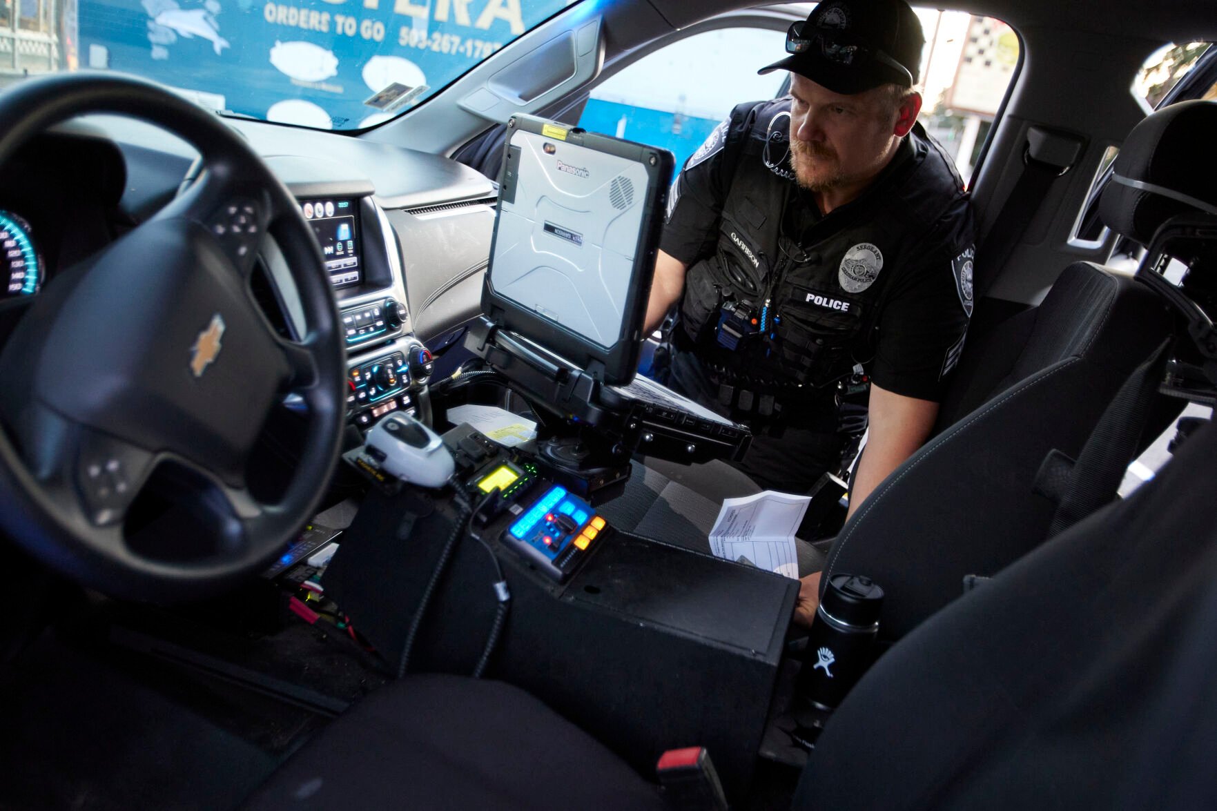 <p>Gresham Police Sgt. Travis Garrison runs an ID and insurance check in Gresham, Ore., Thursday, July 21, 2022. Gresham, a Portland suburb, has seen an increase in fatal shootings and gun violence at the same time as it has a shortage of officers. </p>