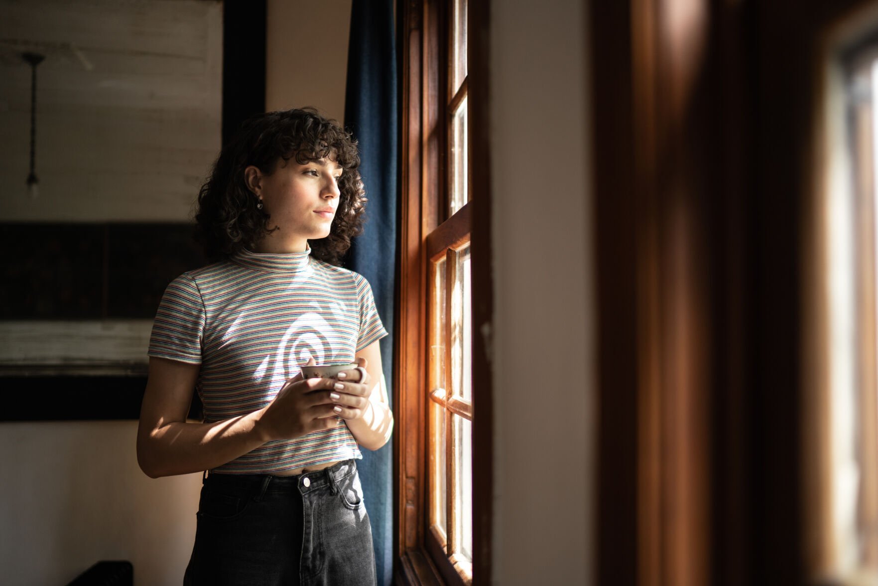 <p>Transgender woman drinking tea looking through the window at home</p>