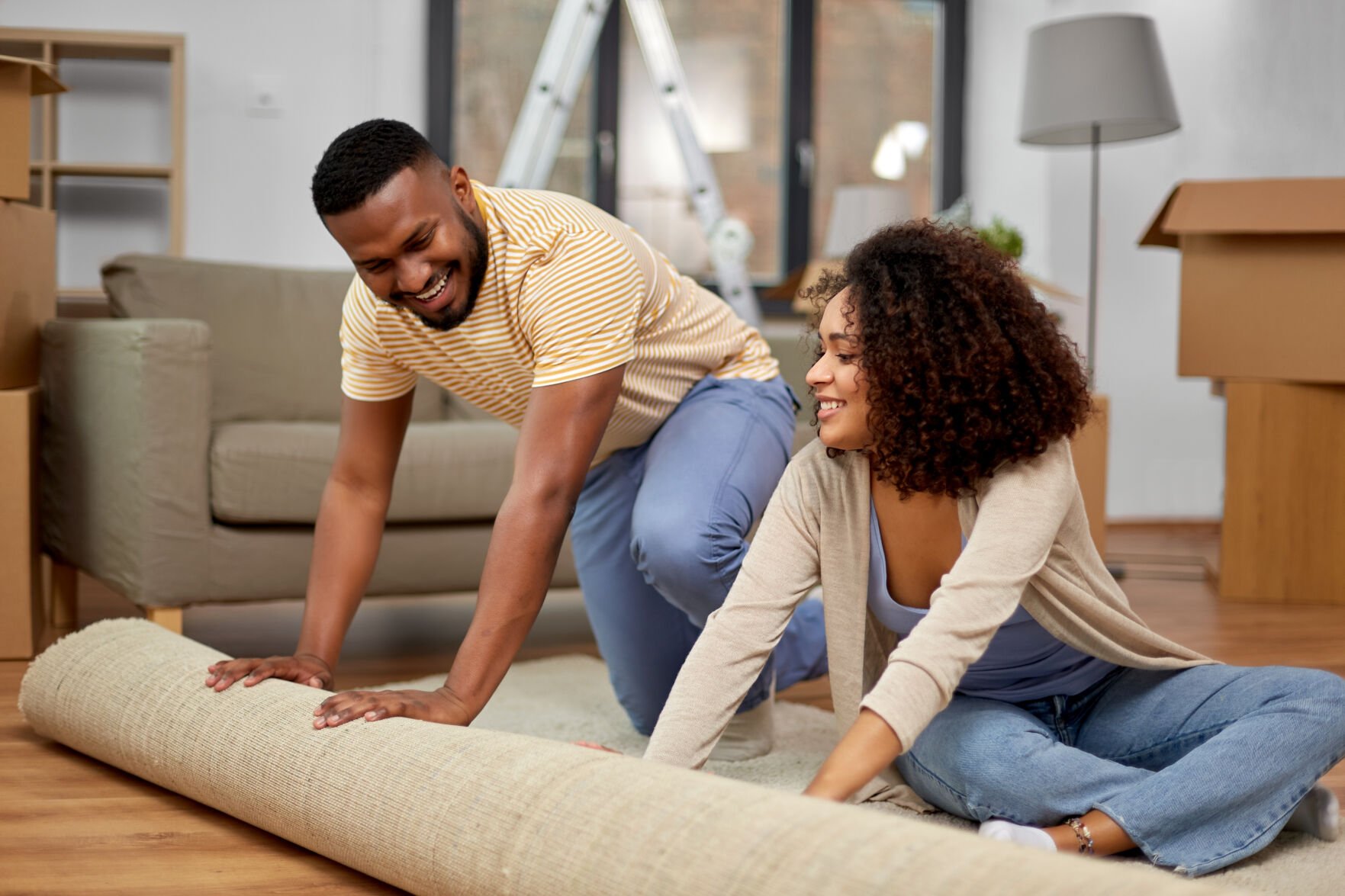 <p>moving, people, repair and real estate concept - happy african american couple with carpet at new home</p>