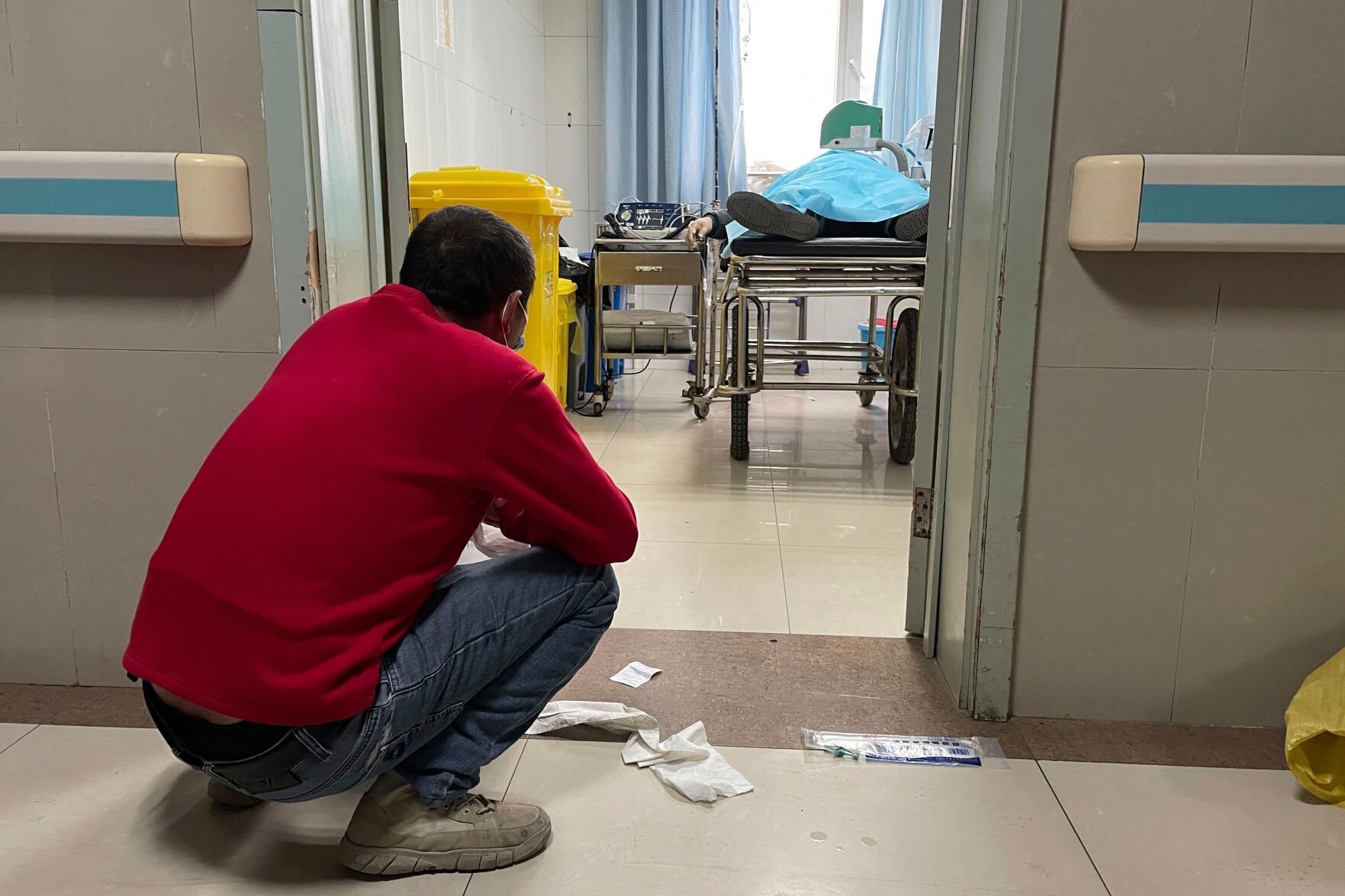 <p>A man squats outside a treatment room Dec. 21 as an elderly person receives help with breathing via a manual ventilator pump at the emergency department of the Baoding No. 2 Central Hospital in Zhuozhou city of Baoding prefecture in northern China's Hebei province.</p>