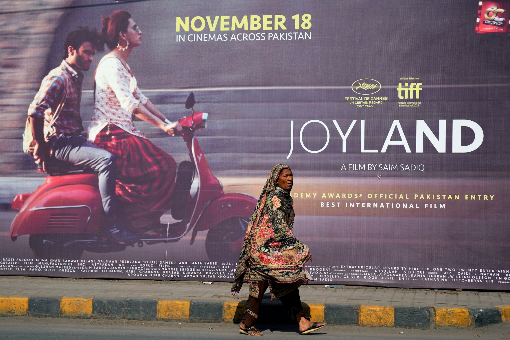 <p>A woman walks past a promotion for the movie "Joyland" displayed Nov. 17 outside a cinema in Lahore, Pakistan. The Pakistani movie caused an uproar for its depiction of a relationship between a married man and a trans woman, but it also shone a spotlight on the country's transgender community.</p>