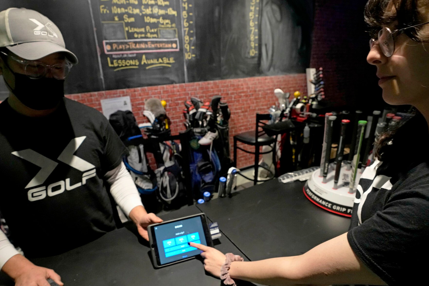 <p>X-Golf manager J.W. Park, left, helps Ashley Moreno to check out at X-Golf indoor golf in Glenview, Ill., Friday, Jan. 20, 2023. </p>