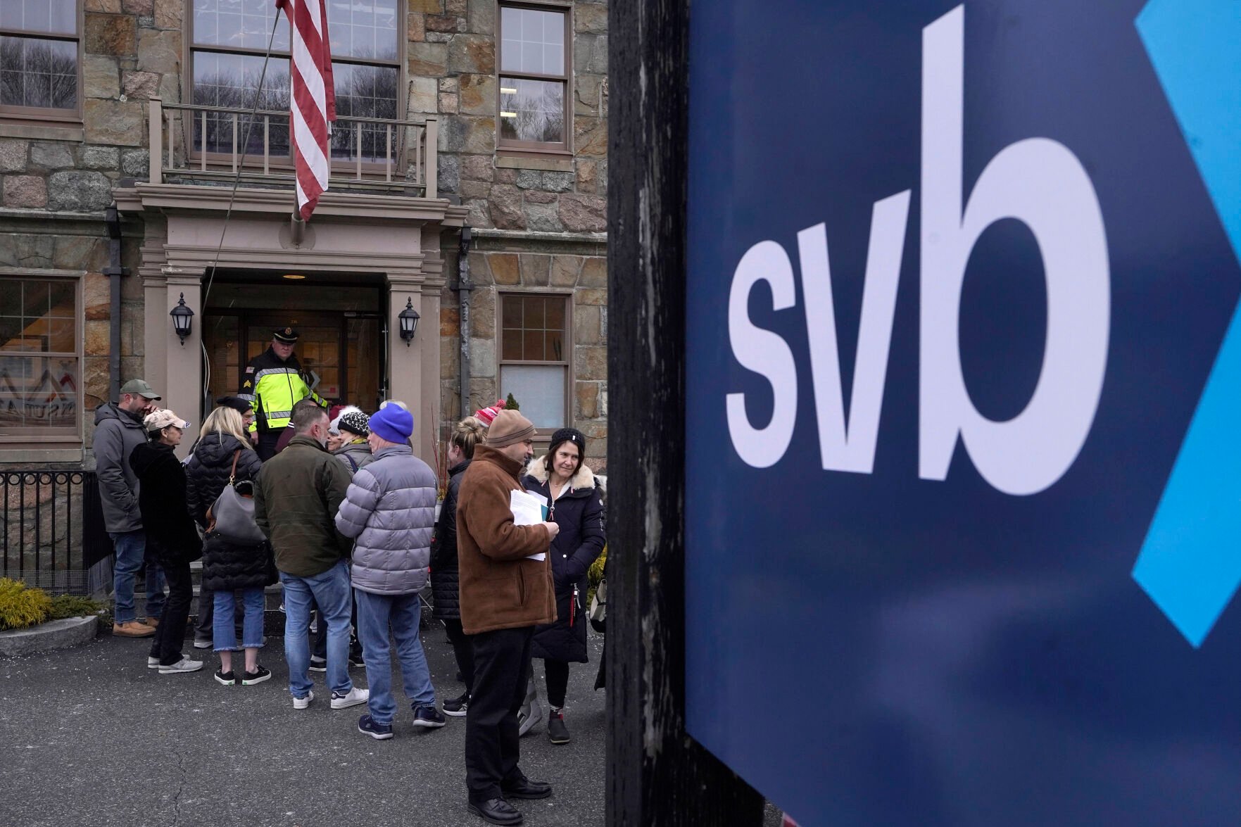 <p>A law enforcement official stands in an entryway to a Silicon Valley Bank branch location March 13 as customers and bystanders line up in Wellesley, Mass.</p>