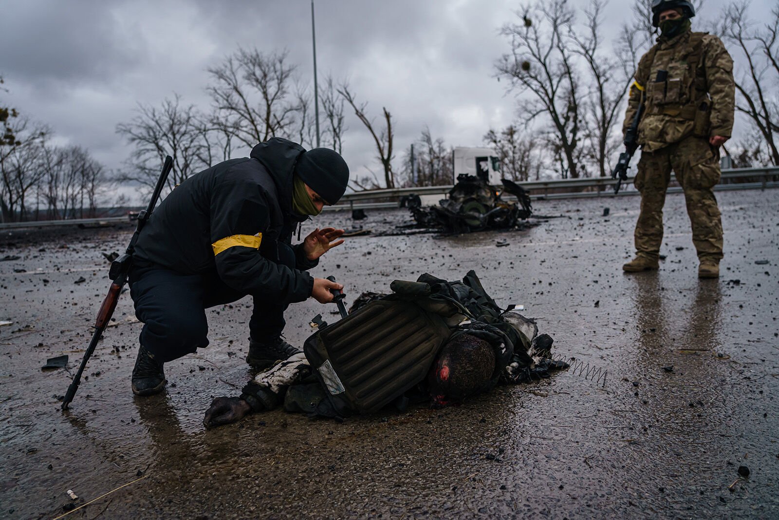 <p>Ukrainian soldiers salvage equipment off the body of a dead Russian soldier after a Russian vehicle was violently destroyed by Ukrainian forces in a battle along the main road March 3 near Sytnyaky, Ukraine.</p>