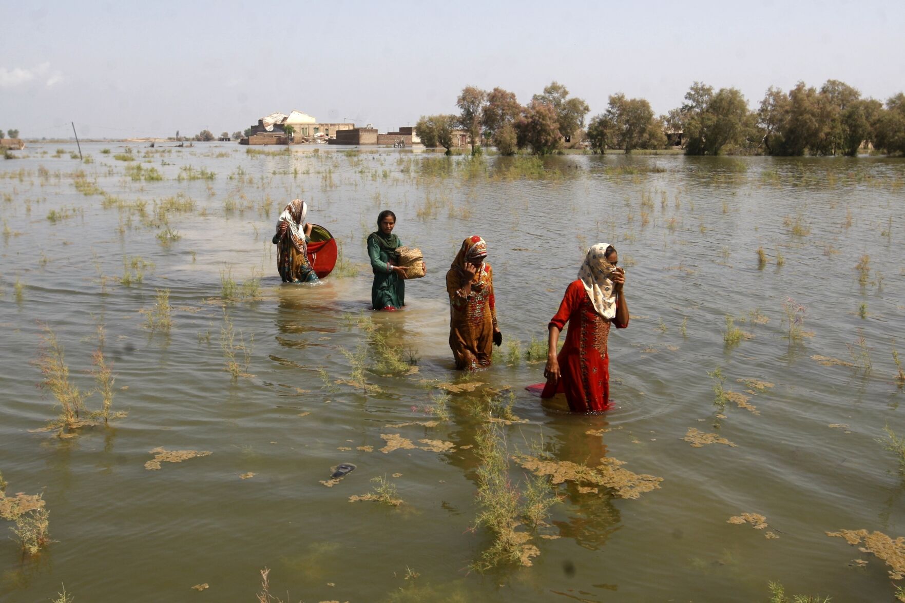 <p>Pakistani women wade through floodwaters as they take refuge Sept. 2, 2022, in Shikarpur district of Sindh Province, Pakistan.</p>