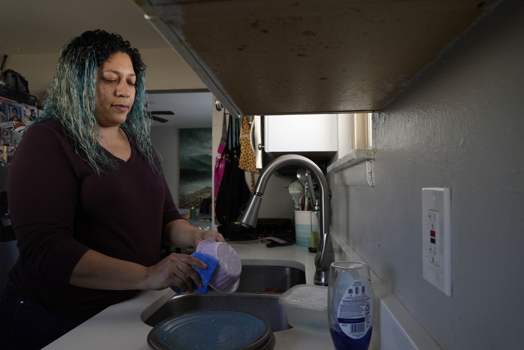 <p>Betty Rivas cleans dishes using tap water Feb. 23 in Commerce City, Colo. Rivas was startled by a letter telling her that the drinking fountains her 8-year-old used at school weren't safe. Her family is one of many in the community who do not drink the tap water and instead buy water from potable refill stations around town.</p>