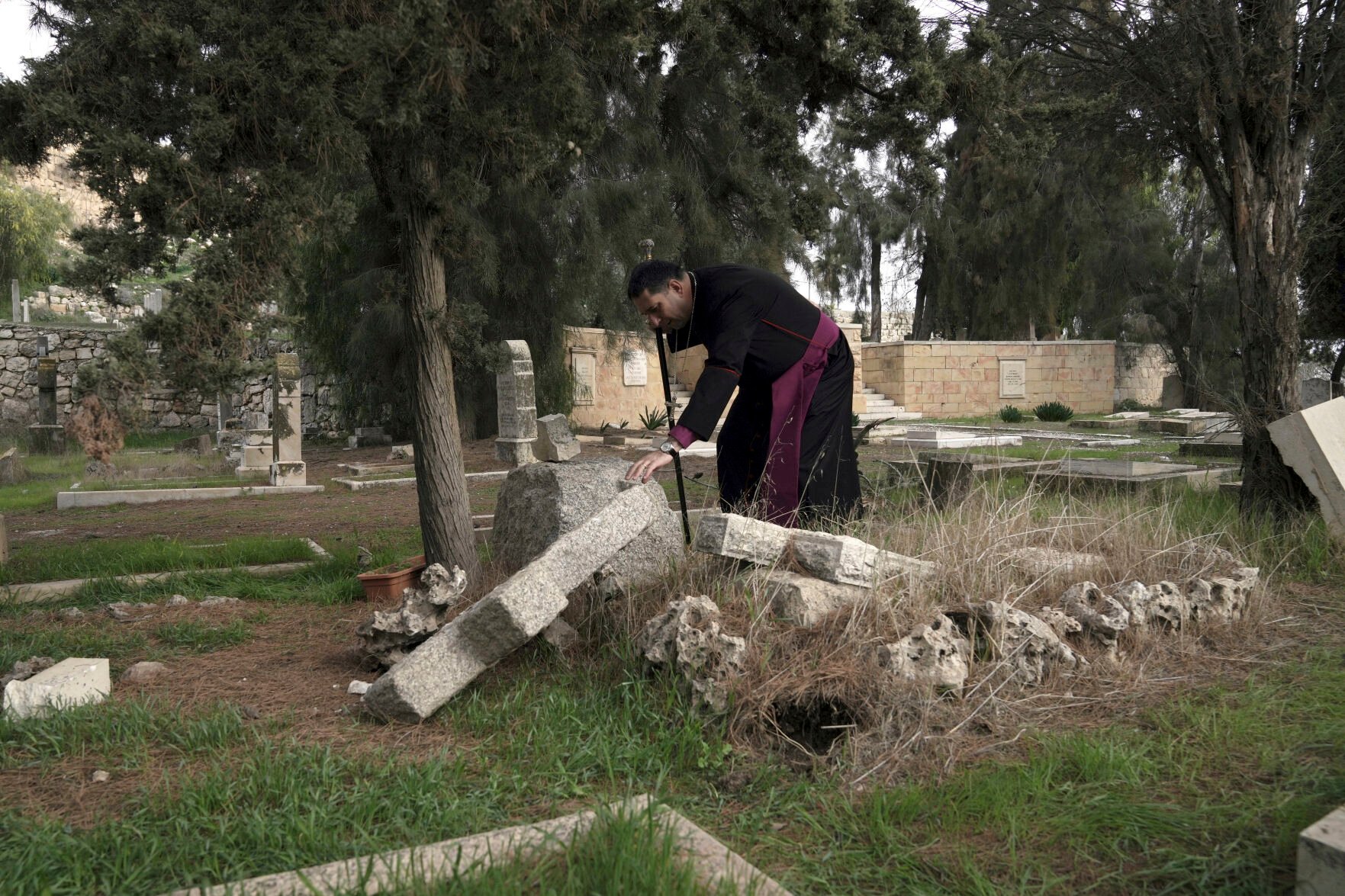 <p>Hosam Naoum, a Palestinian Anglican bishop, looks at a damaged grave at a historic Protestant Cemetery where vandals desecrated more than 30 graves, on Jan. 4 on Jerusalem's Mount Zion.</p>