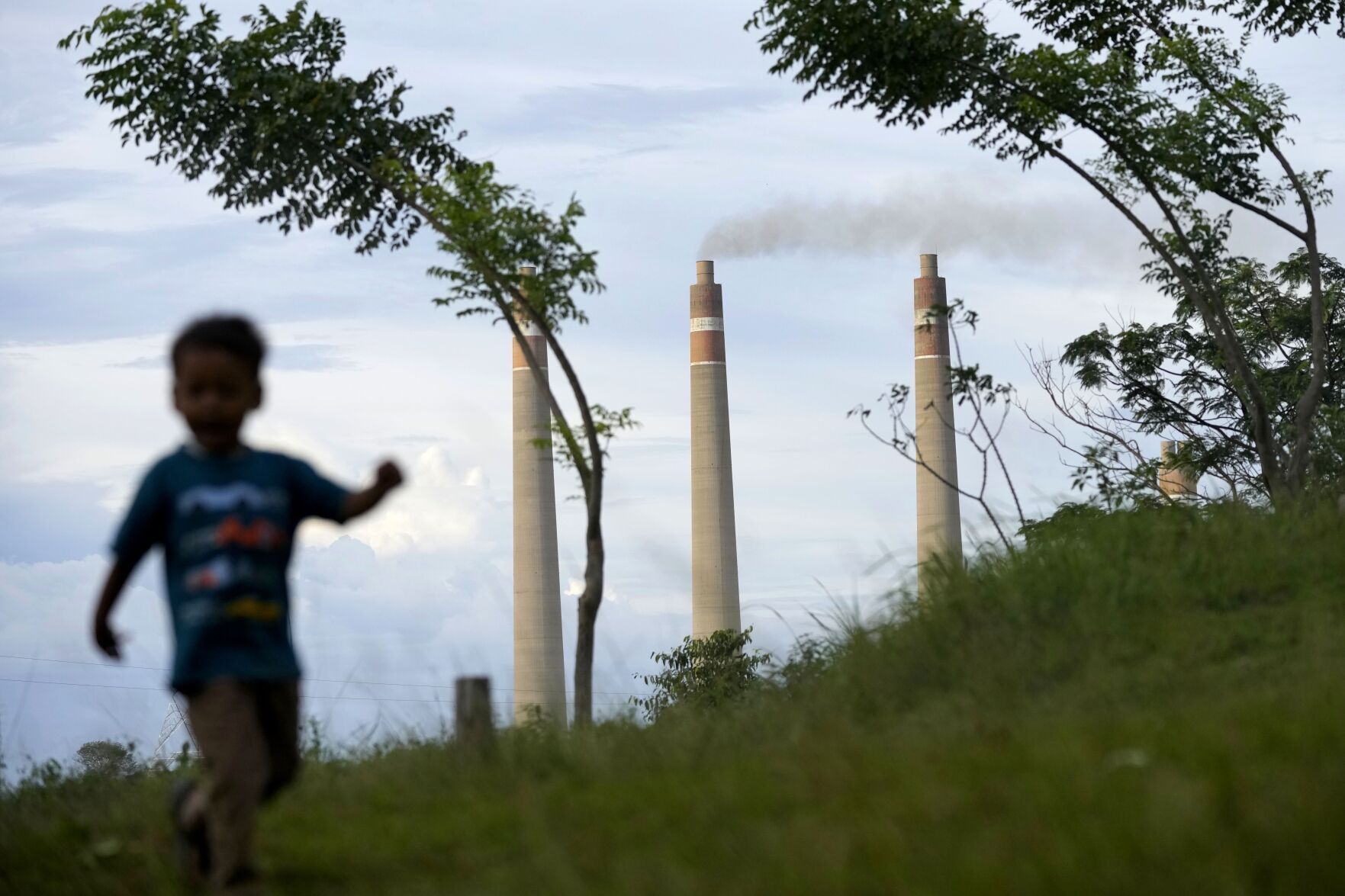 <p>A young boy plays on a hill called "Teletubbies Hill," a locally popular tourist attraction, as the chimneys of Suralaya coal power plant loom in the background, Jan. 8 in Cilegon, Indonesia.</p>