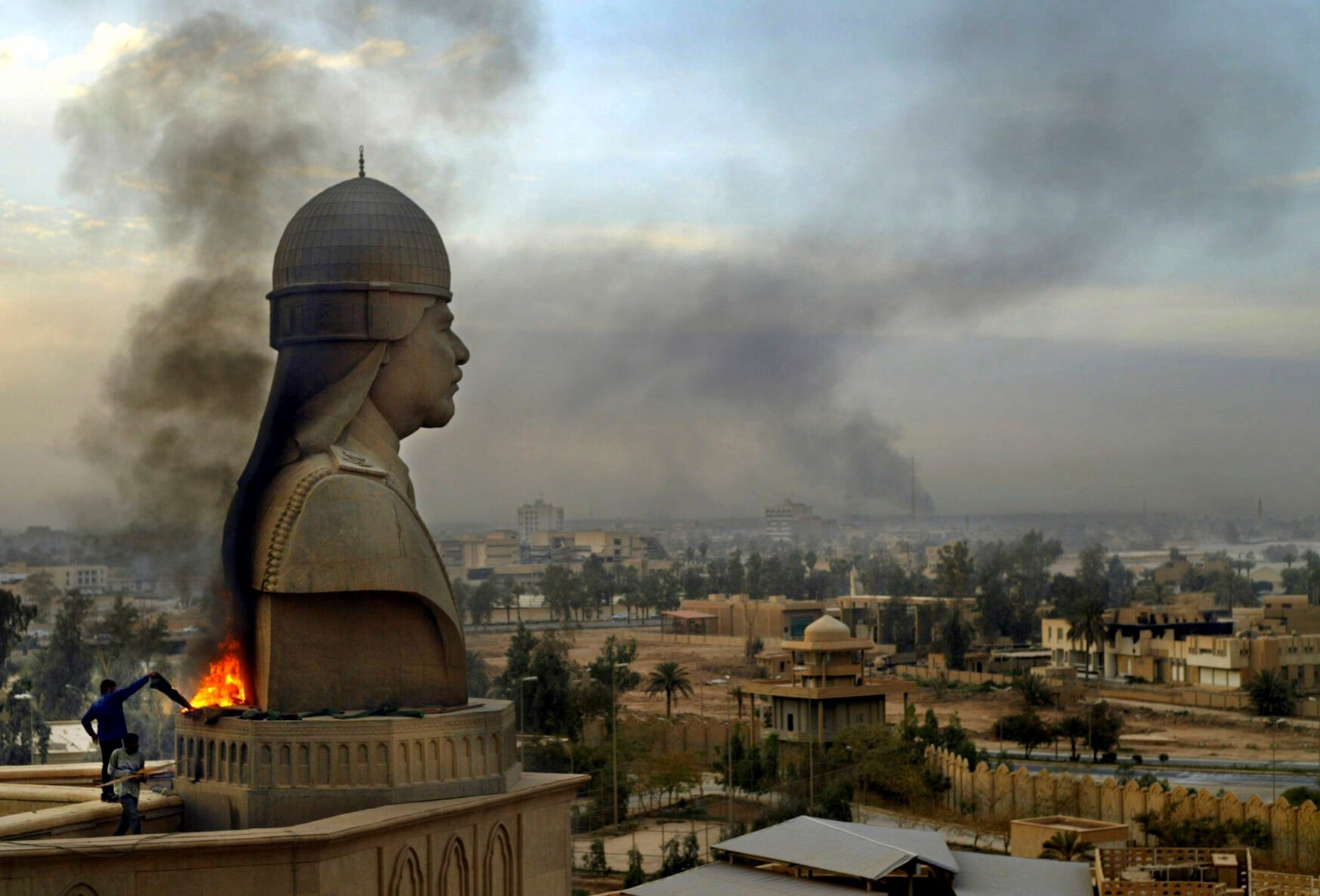 <p>Smoke billows from the base of a sculpture depicting Iraqi President Saddam Hussein April 13, 2003, after looters set it on fire atop the roof of his Al-Salam Presidential Palace in Baghdad.</p>