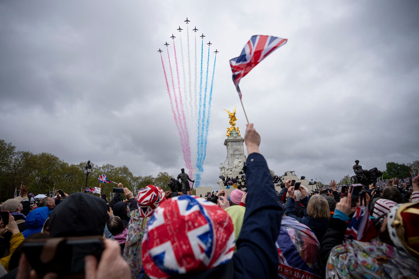 <p>People watch the Royal Air Force fly past as Britain's King Charles III and Queen Camilla wave to the crowd from the balcony of Buckingham Palace after the coronation ceremony Saturday in London.</p>