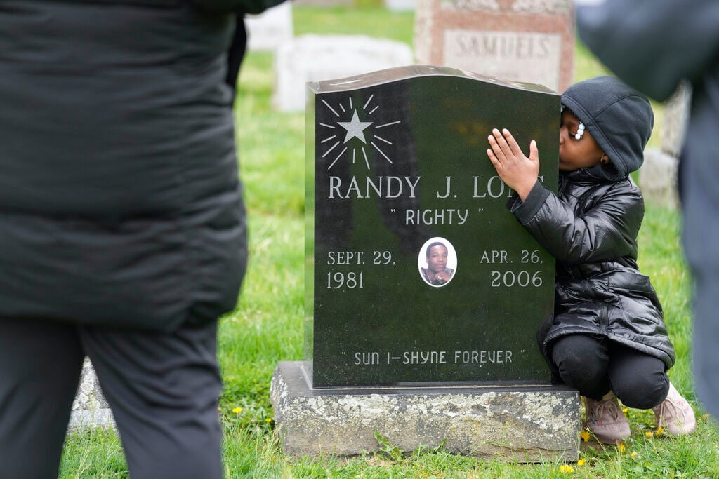 <p>Xia'la Long kisses her uncle Randy Long's tombstone while posing for a picture for her mother, Tamara Long, and grandmother, Debra Long, in Poughkeepsie, N.Y., April 19, 2023. An AP examination of data from 23 states shows that Black people are disproportionately denied aid from programs that reimburse victims of violent crime. (AP Photo/Seth Wenig)</p>