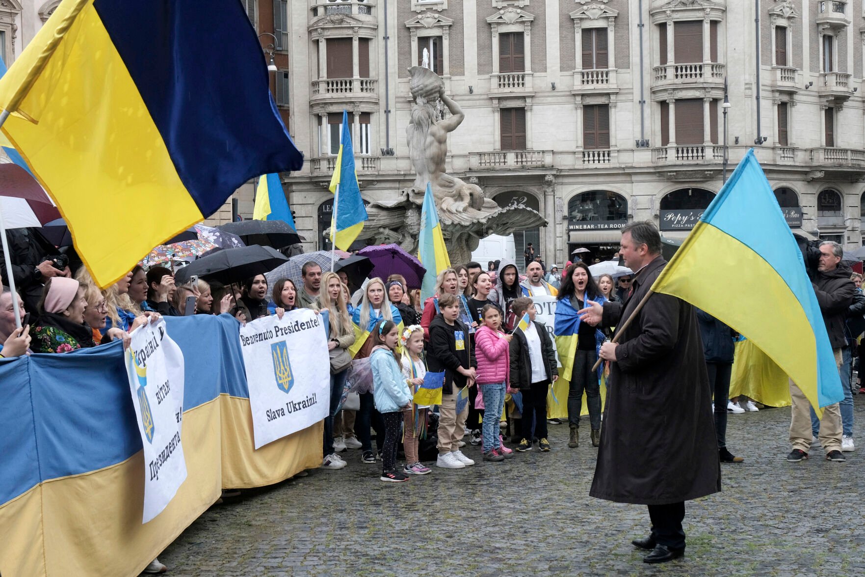 <p>People holding Ukrainian flags and a sign reading "Welcome President. Glory to Ukraine" gather for the motorcade of Ukrainian President Volodymr Zelenskyy on Saturday in downtown Rome.</p>
