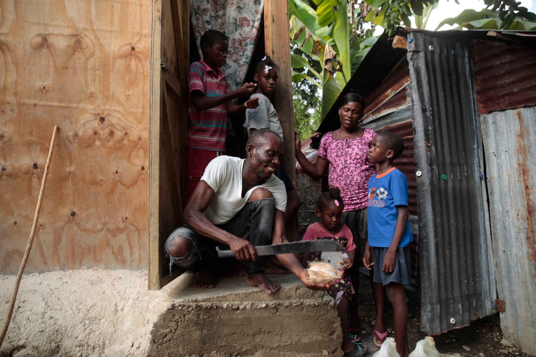 <p>Mackenson Victor opens a coconut for his daughter Manouchi Victor, front center, and stepchildren Myson Veillard, top left, Routcheland Veillard, top, second from left, and Dabens Veillard, front right, as his partner Renese Esteve looks on at their home May 25 in a rural area of Saint-Louis-du-Sud, Haiti.</p>