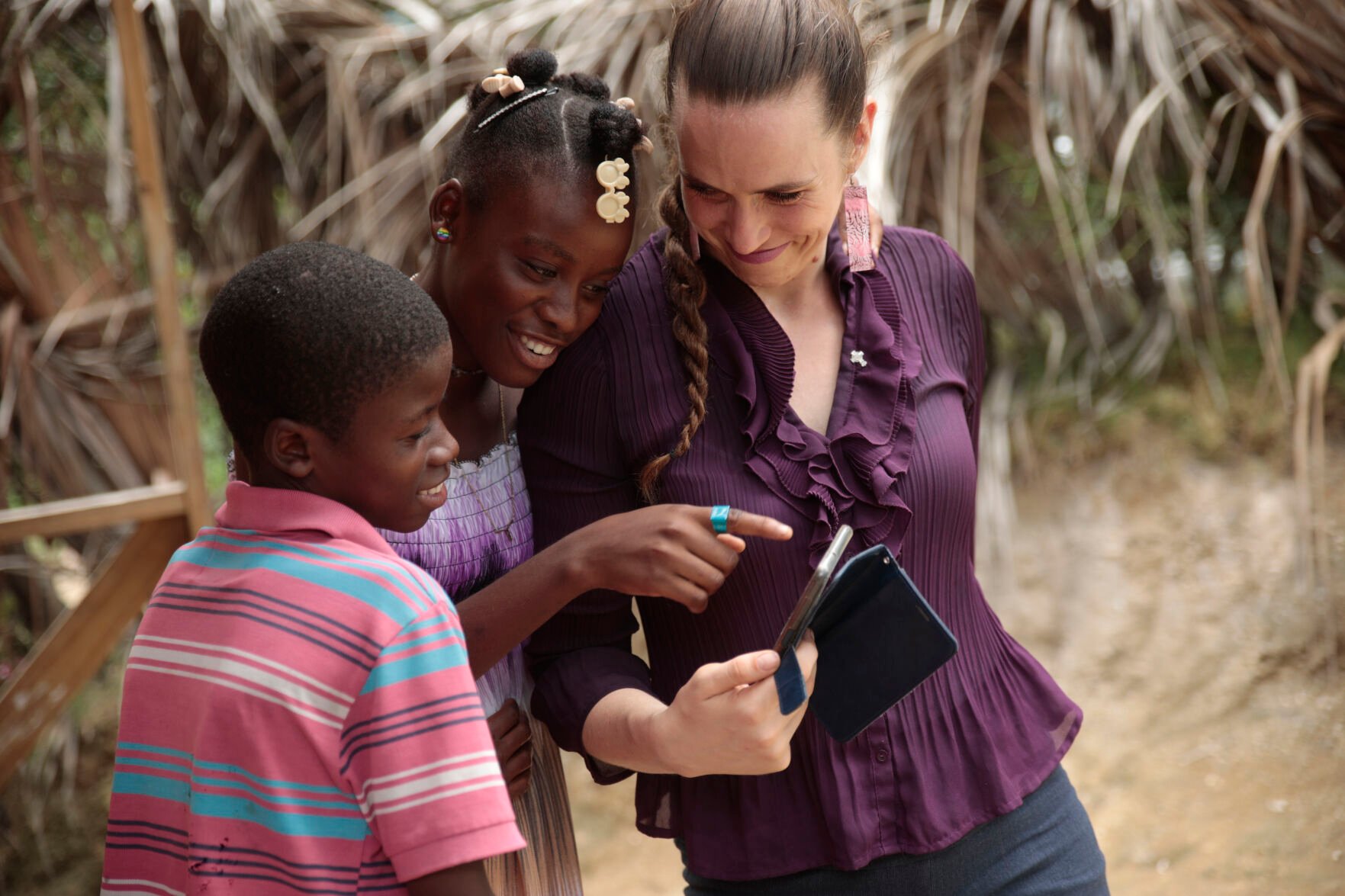 <p>Siblings Mylouise Veillard, center, and Myson look at pictures on a phone with Morgan Wienberg on May 25 in a rural area of Saint-Louis-du-Sud, Haiti. Wienberg is executive director of Little Footprints, Big Steps, a nonprofit that helped reunite the siblings with their mother.</p>