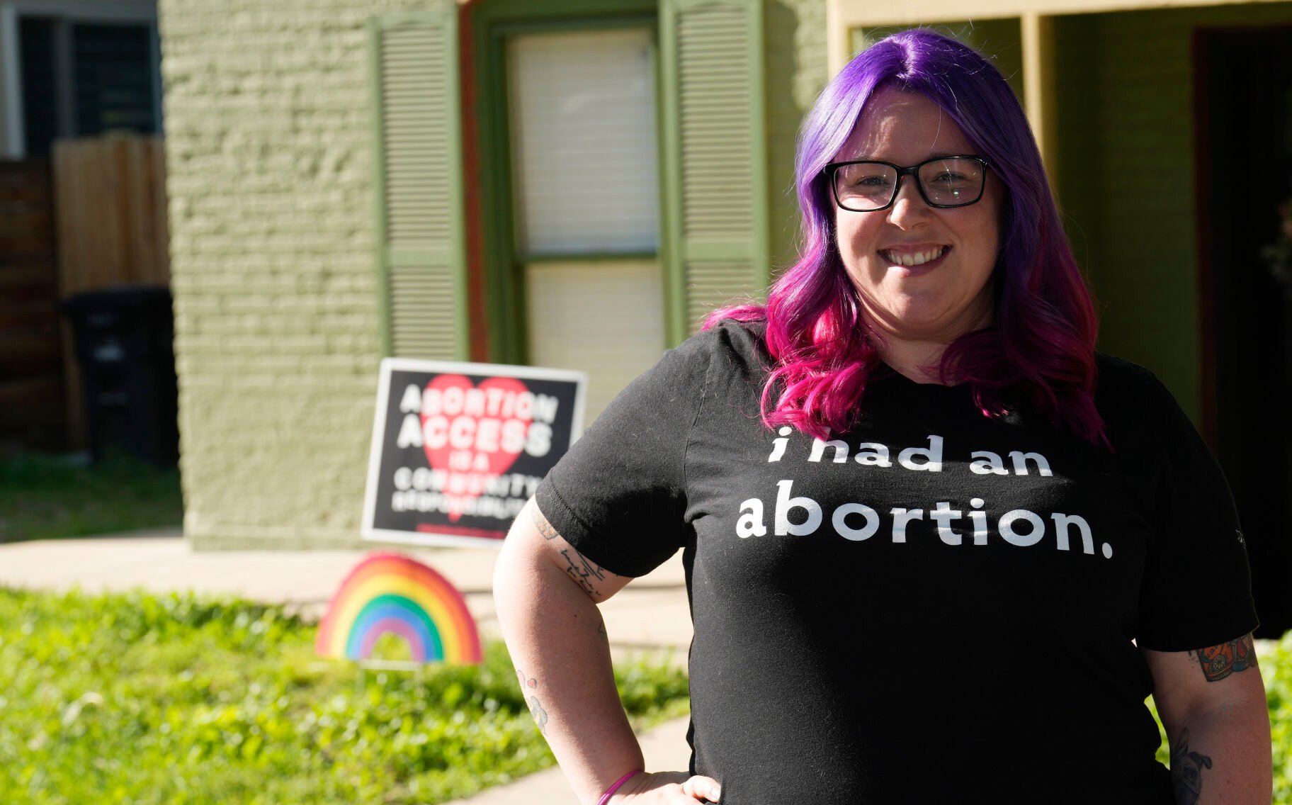 <p>Leah Dean, a native of the Texas panhandle, poses outside her home Monday in Denver. She and her partner found a place in Colorado, where their LGBTQ+ pride flag flies above the banner in front of their house that proclaims “Abortion access is a community responsibility."</p>