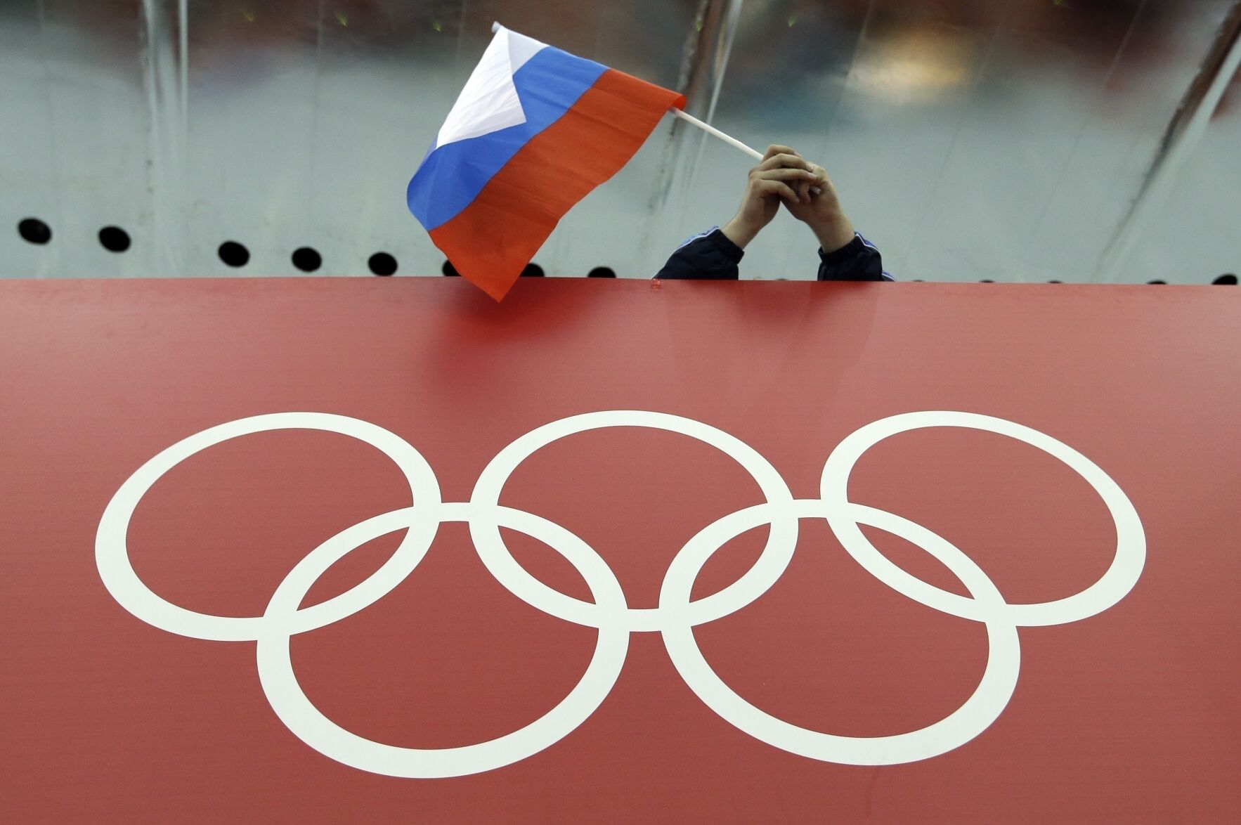 <p>A Russian flag is held above the Olympic Rings at Adler Arena Skating Center during the 2014 Winter Olympics in Sochi.</p>