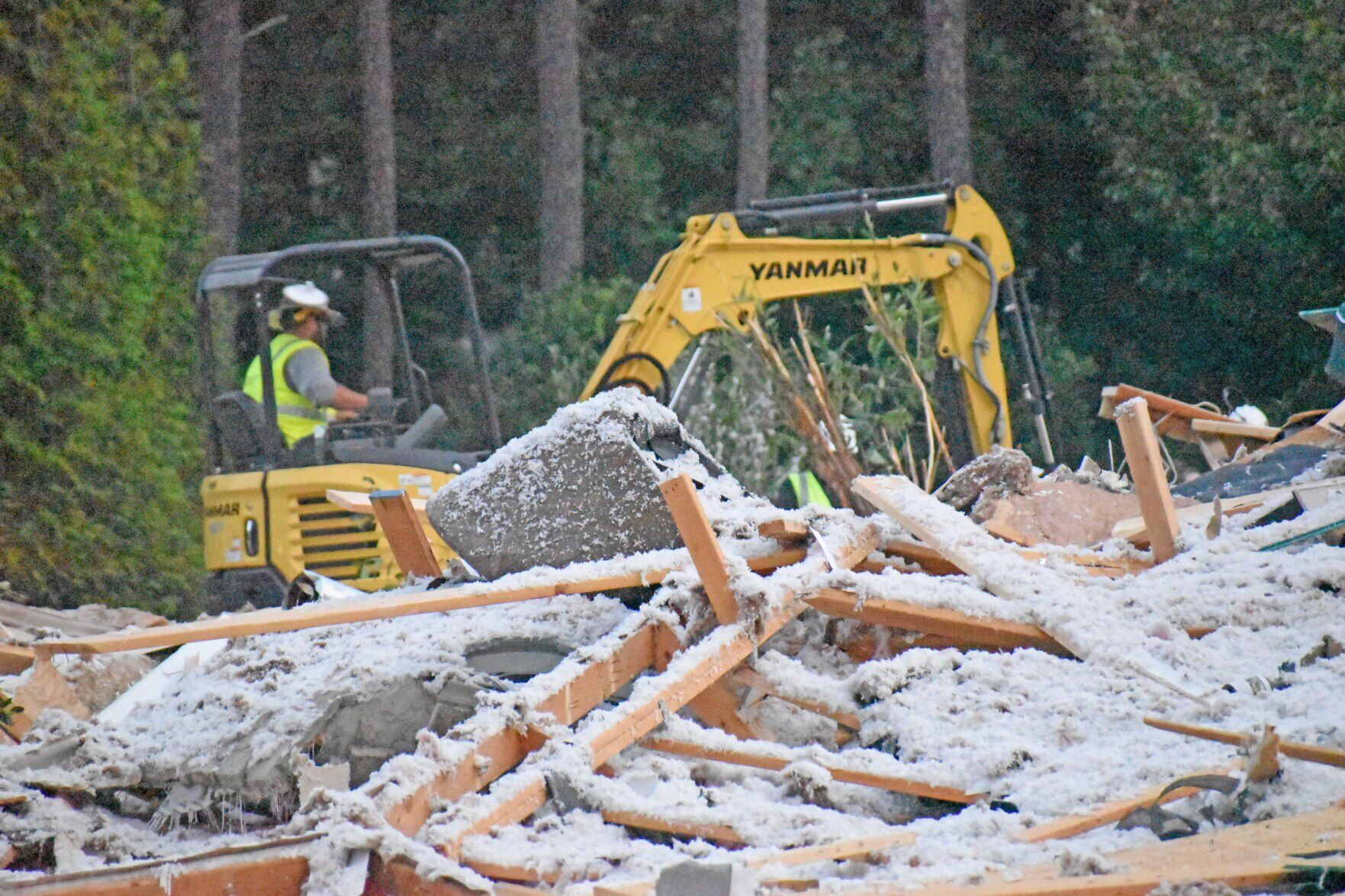 <p>A pile of timber and insulation sits in front of an excavator at the scene of a home explosion on Barber Loop.</p>
