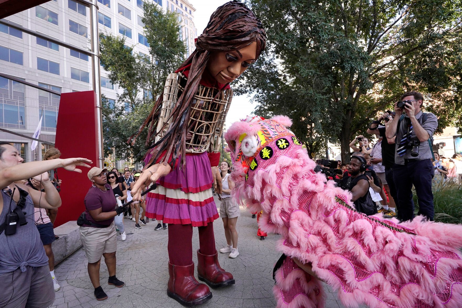 <p>Little Amal, a 12-foot puppet of a 10-year-old Syrian refugee girl, center, is greeted Thursday by a performer in a lion dance costume near the Chinatown neighborhood of Boston.</p>