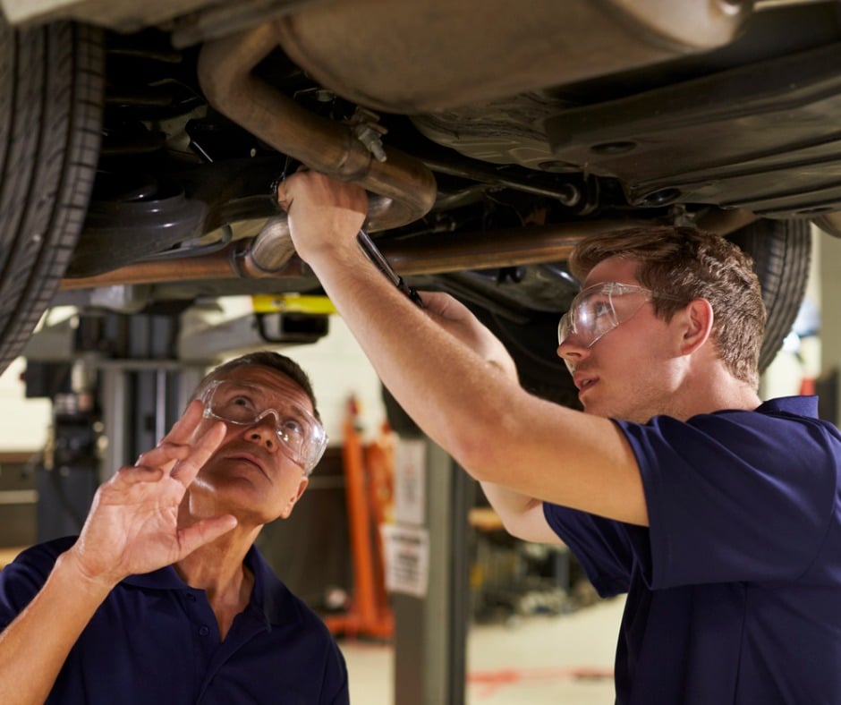 Mechanic And Male Trainee Working Underneath Car Together Picture Id628110734