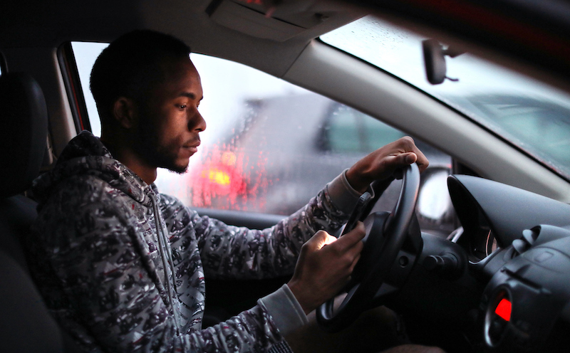 African Man Using His Phone While Driving In The Rain.
