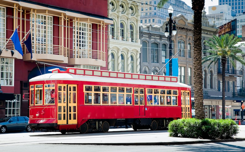 New Orleans Bright Red Streetcar Traveling Amid Palms And Flags