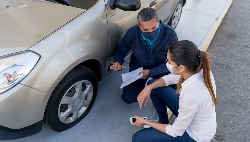 Woman With A Flat Tire Talking To A Mechanic While Wearing A Facemask