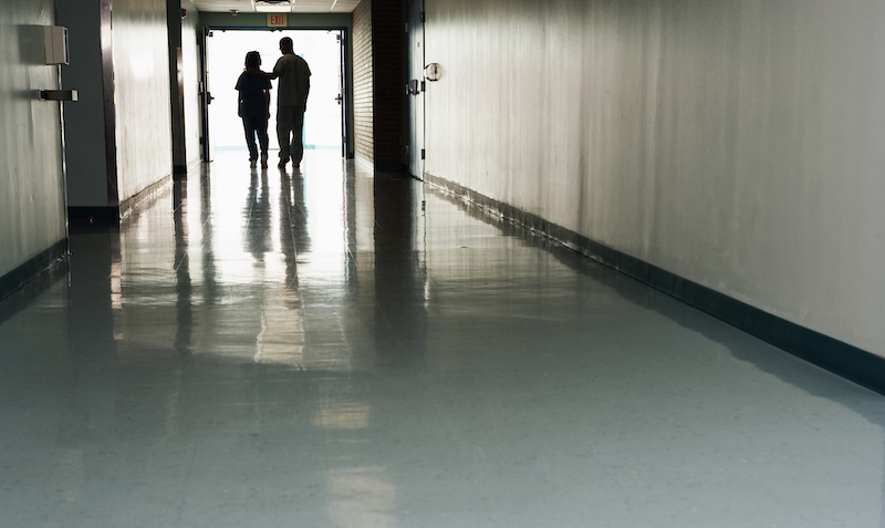 Two People Standing At End Of Corridor In Hospital