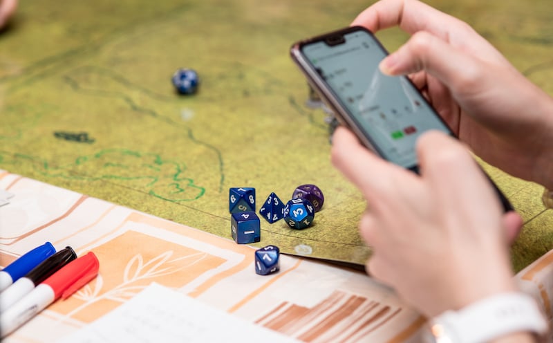 Girl Using The Smartphone During A Role Playing Game Of Dungeons And Dragons. Dices On The Green Battlefield