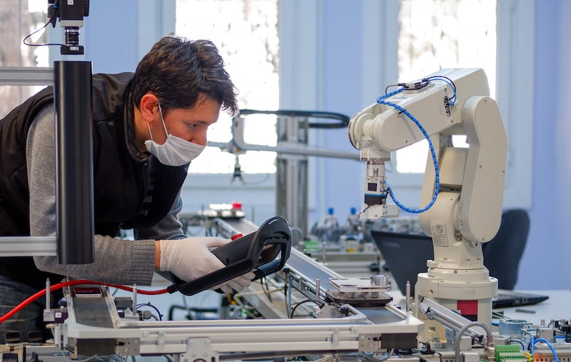 Man With Surgical Mask On Face Against Covid 19 ( Coronavirusis ) Programming Robot Arm With Control Panel Which Is Integrated On Smart Factory Production Line.