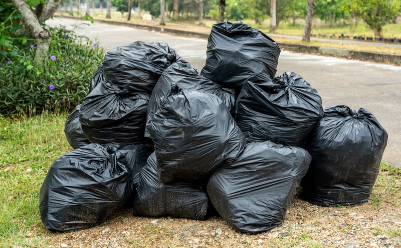 Black Garbage Bags On The Road With Green Grass And Plants Background