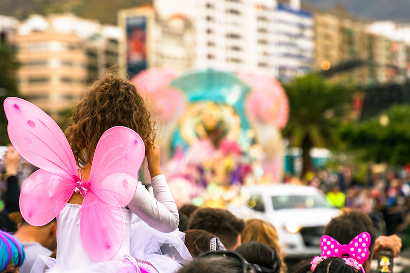 People Looking At The Carnival Party. Pretty Girl Dressed As A Pink Angel In A Carnival Party. Defocused Background Image